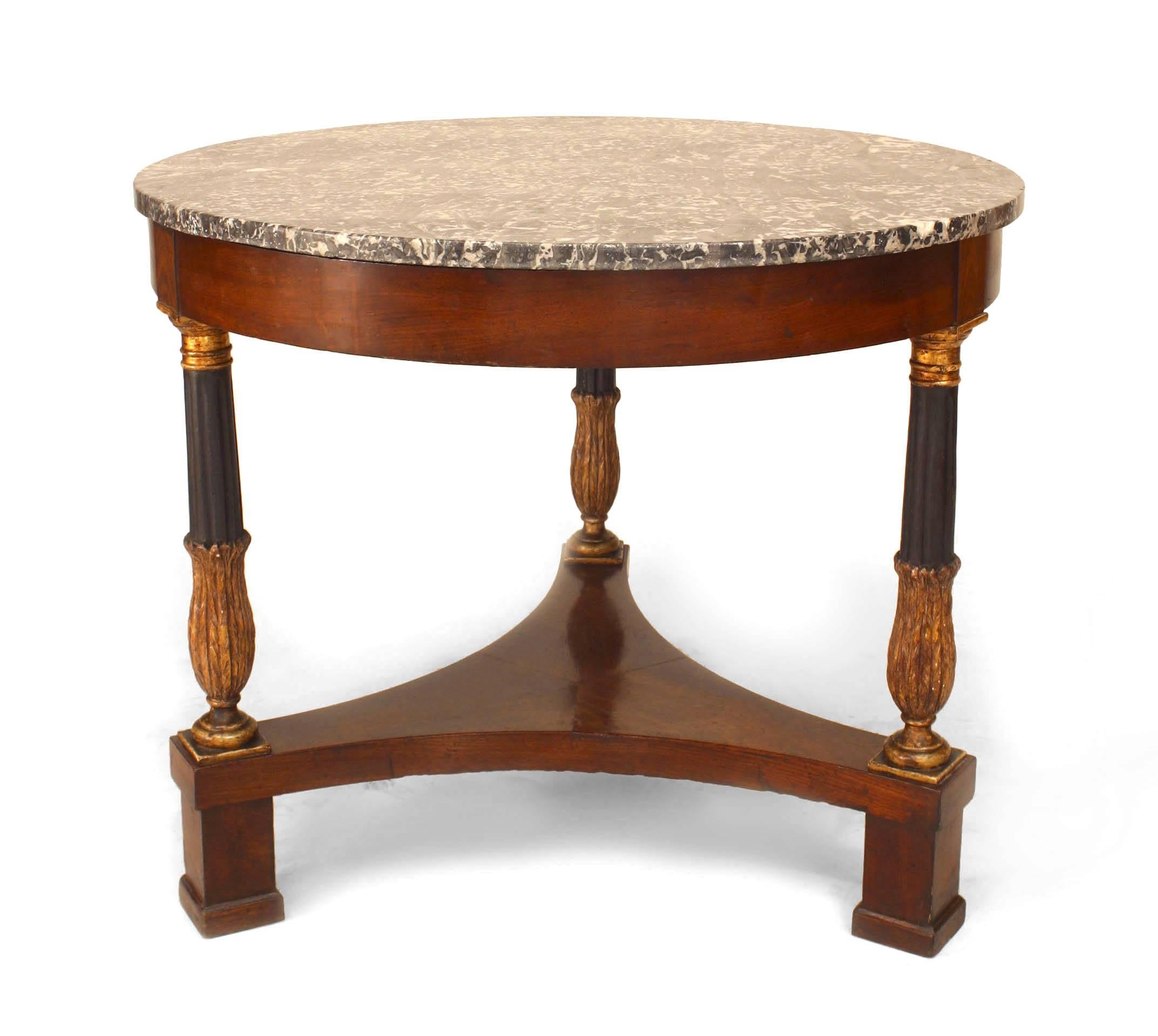 Italian Neoclassic mahogany center table dating to the second quarter of the nineteenth century. The table's round black and grey marble top is supported by three gilt trimmed and ebonized legs spread across an elevated triform stretcher.
