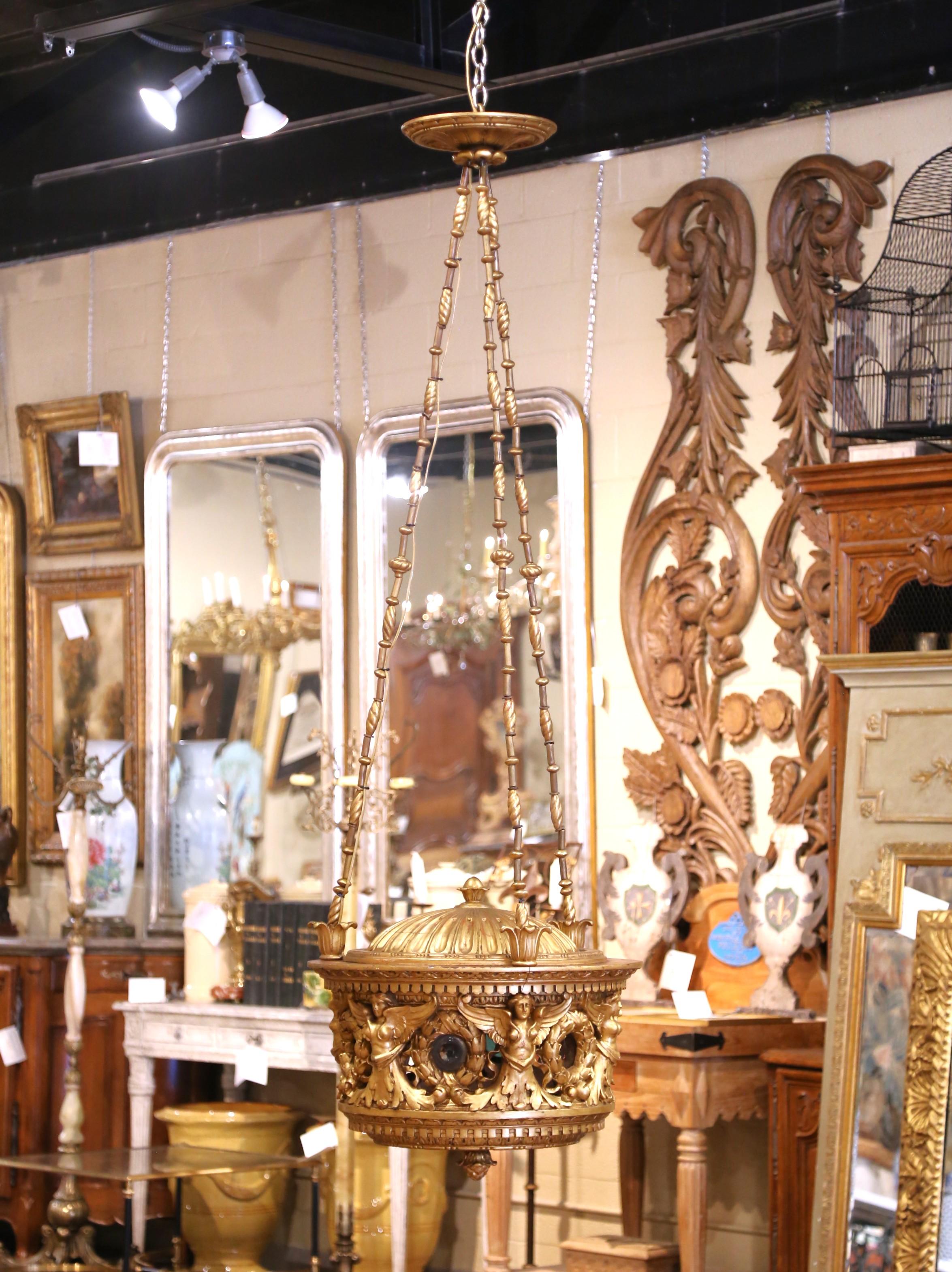Fabriqué en Italie vers 1860, ce lustre exceptionnel en bois doré incarne la grandeur du style néoclassique. Le cadre circulaire est richement orné de figures féminines ailées sculptées à la main, de couronnes de laurier et de guirlandes florales,