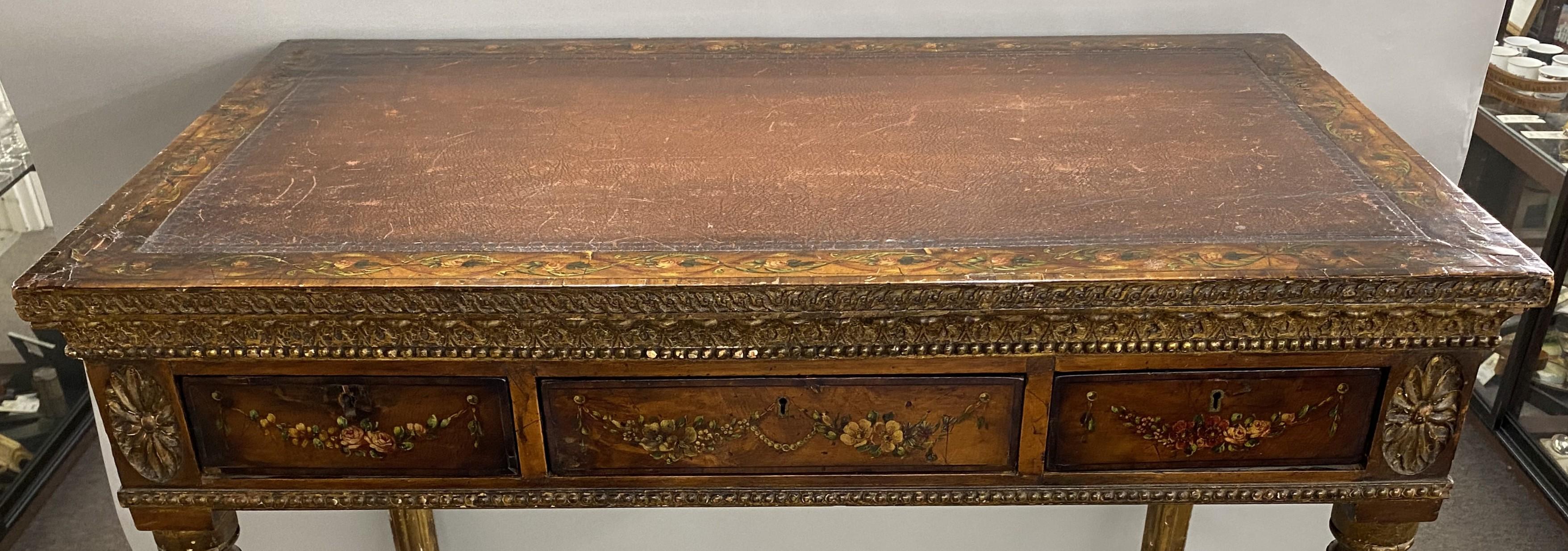 Table à écrire italienne de style néoclassique polychrome peinte à la main, avec une bordure supérieure feuillagée entourant le plateau en cuir brun inséré, et se poursuivant avec un décor de guirlandes feuillagées sur les trois façades de tiroirs à