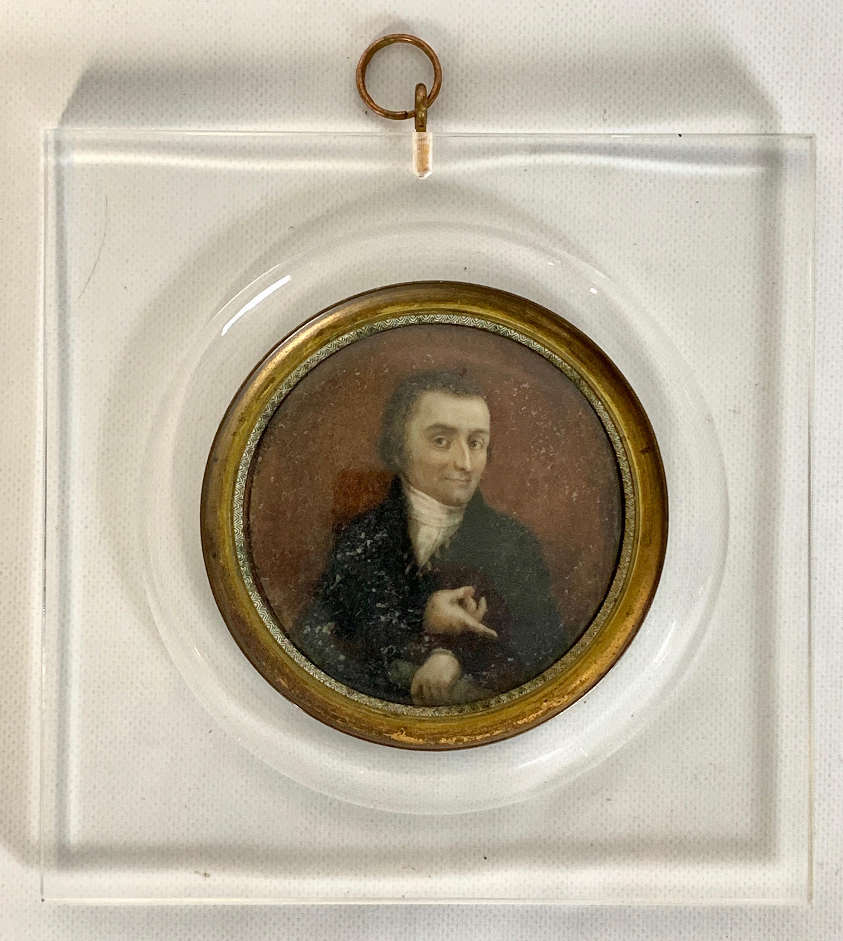 An early 19th century Italian portrait miniature of a gentleman in a black coat pointing downward. Set in a later Lucite frame.