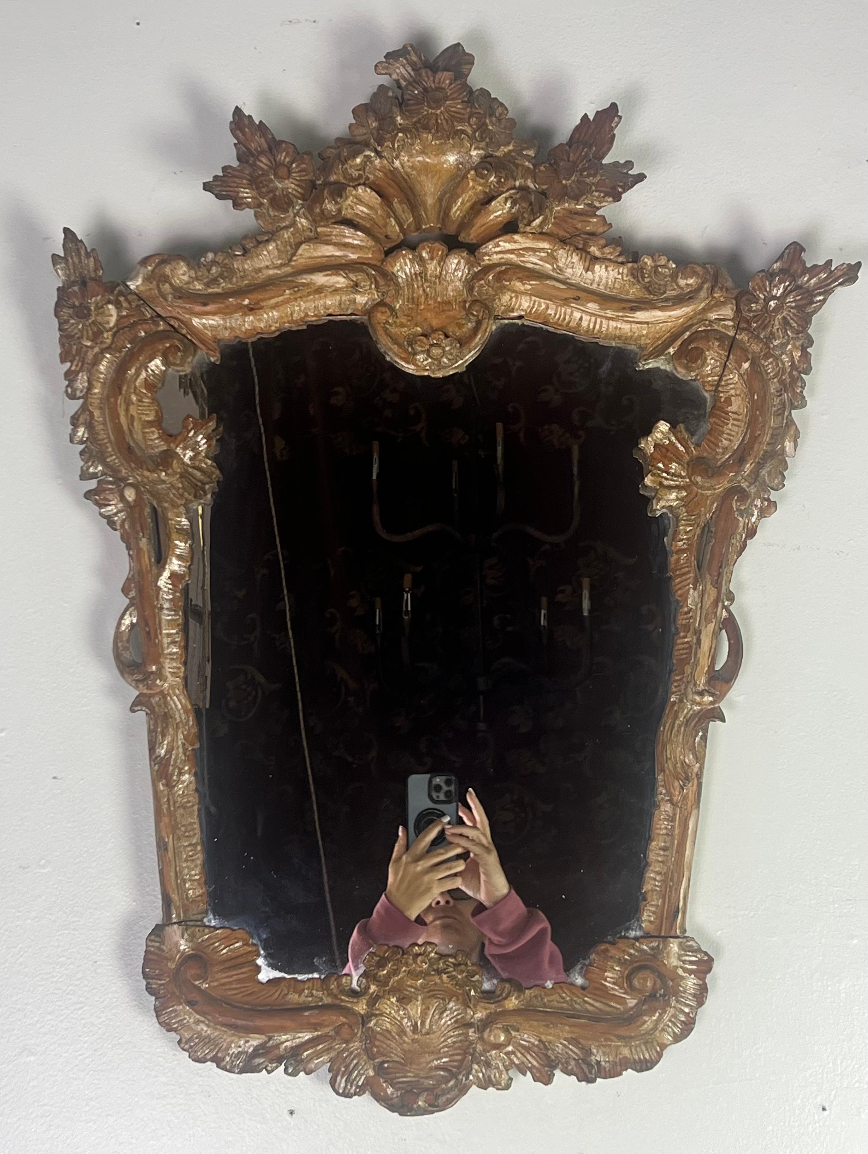 19th C. Italian mirror with a highly ornate and elaborate frame, characteristic of the Rococo style.  The frame is gilded and featured extensive carvings with a rich floral motif.  The top of the mirror showcases a central crest adorned with floral