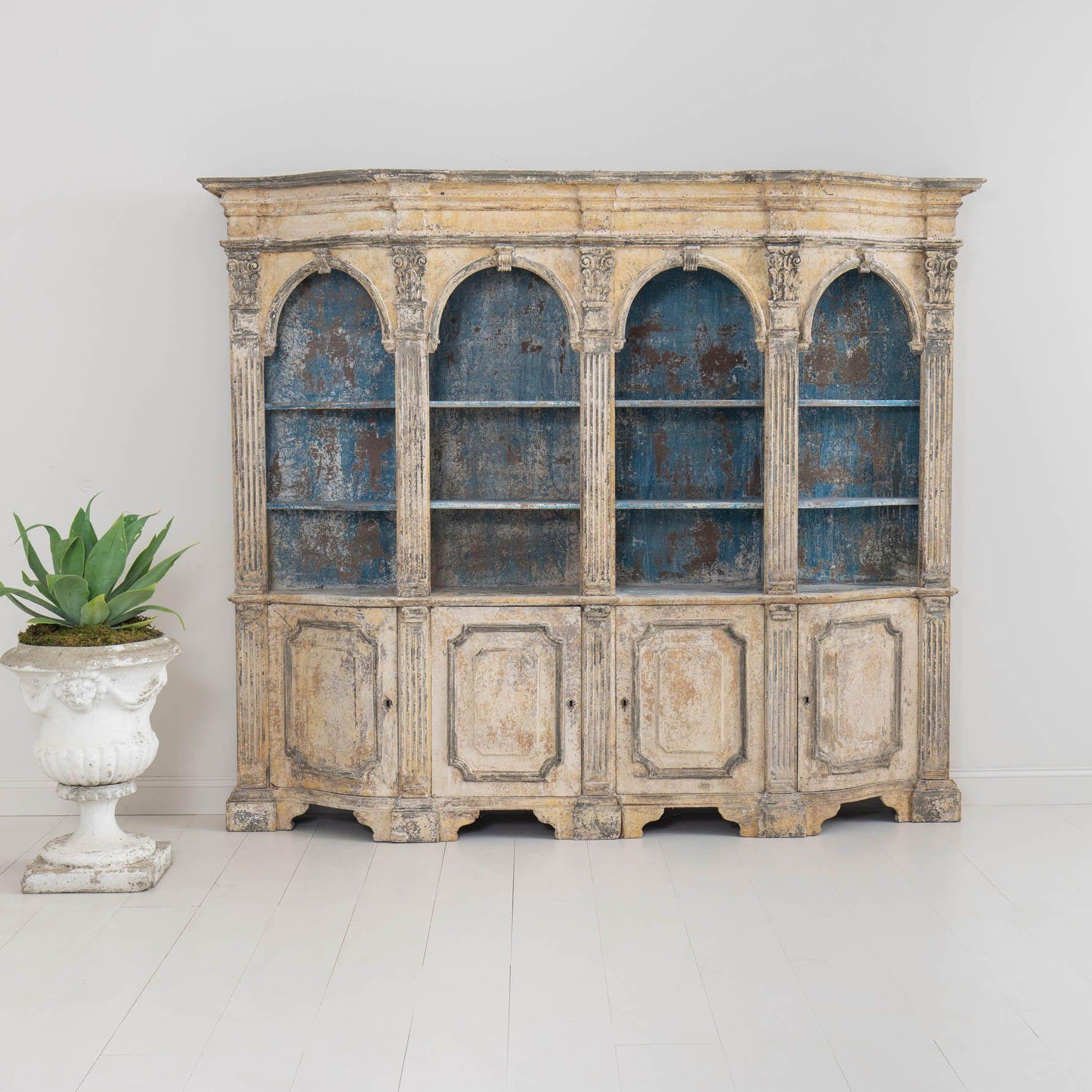 An incredible 19th century Italian Neoclassical style bookcase with a serpentine shape in original paint. Circa 1860. The carved and shaped crown sits above four arched openings with two, fixed shelves flanked by fluted pilasters adorned with