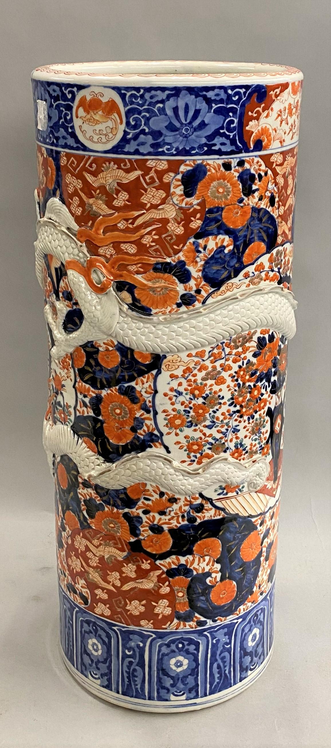 A fine Japanese Imari stick stand or umbrella stand in blue, gilt, and iron red tones with bird and foliate decoration, as well as a relief white dragon with gilt highlights wrapping around the exterior of the cylinder. The stand dates to the late