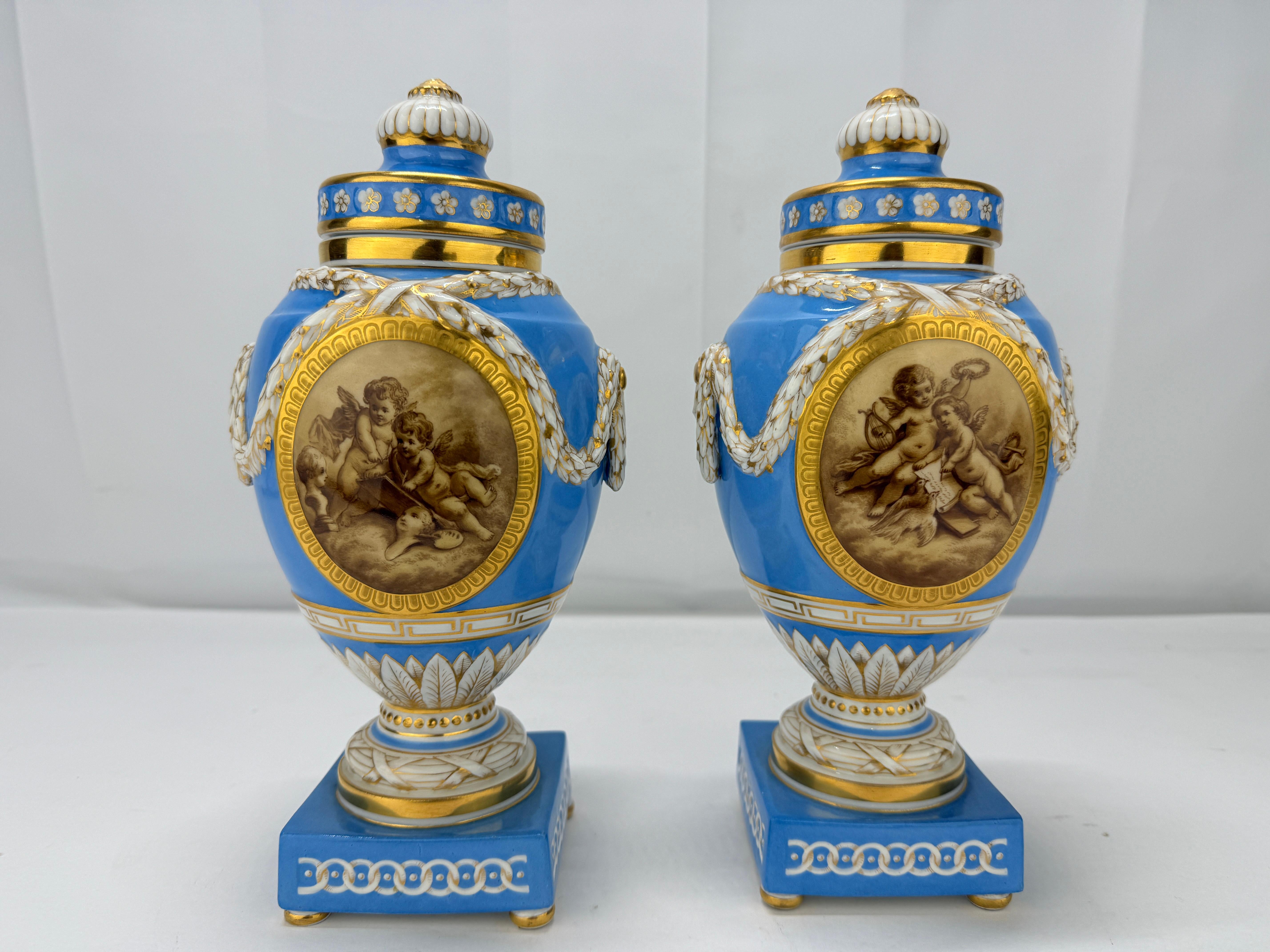 This exquisite pair of 19th-century lidded urns, crafted by the esteemed Königliche Porzellan-Manufaktur (KPM) of Berlin, is a remarkable example of Neoclassical porcelain artistry.

Each urn features a striking celestial blue ground, with