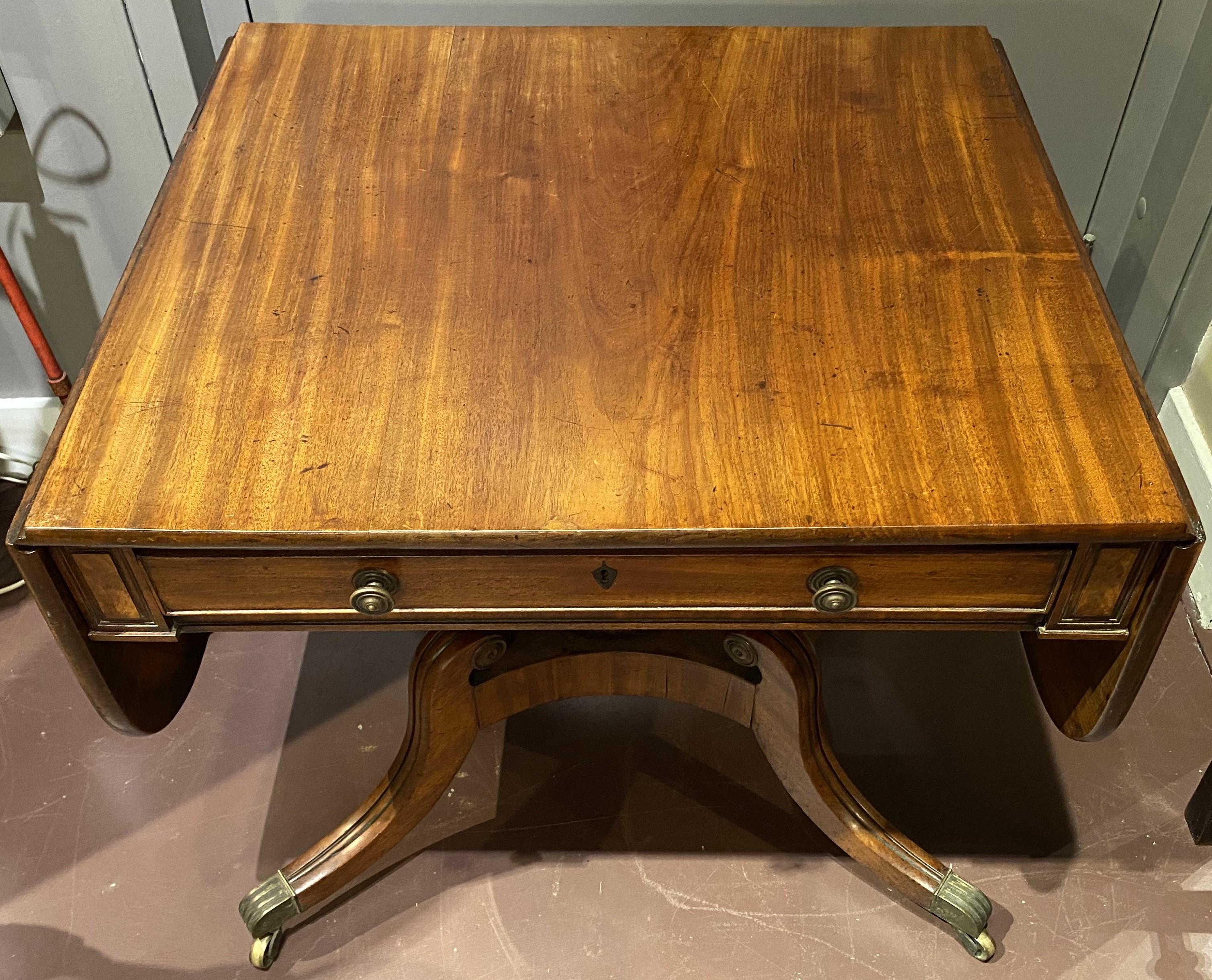 A fine example of a Georgian mahogany drop leaf table with a single frieze drawer, adorned with round brass pulls and an inlaid escutcheon, faux drawer on verso, opening to a rectangular top with rounded corners, all supported by a center turned