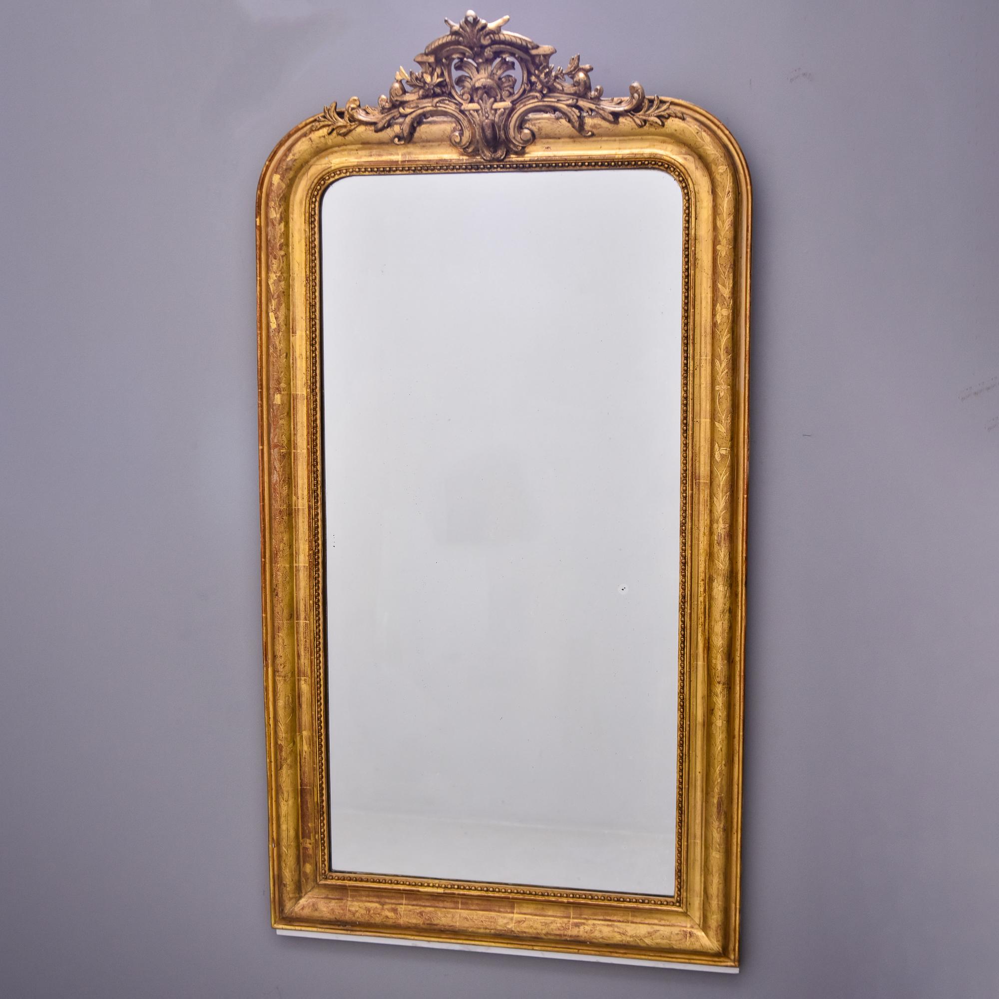 Found in France, this crested Louis Philippe giltwood mirror dates from the 1860s. Frame has a subtle etched leaf and vine design all around, an inner beaded edge and a detailed, open work crown. Mirror is old and has some small foggy spots. Unknown