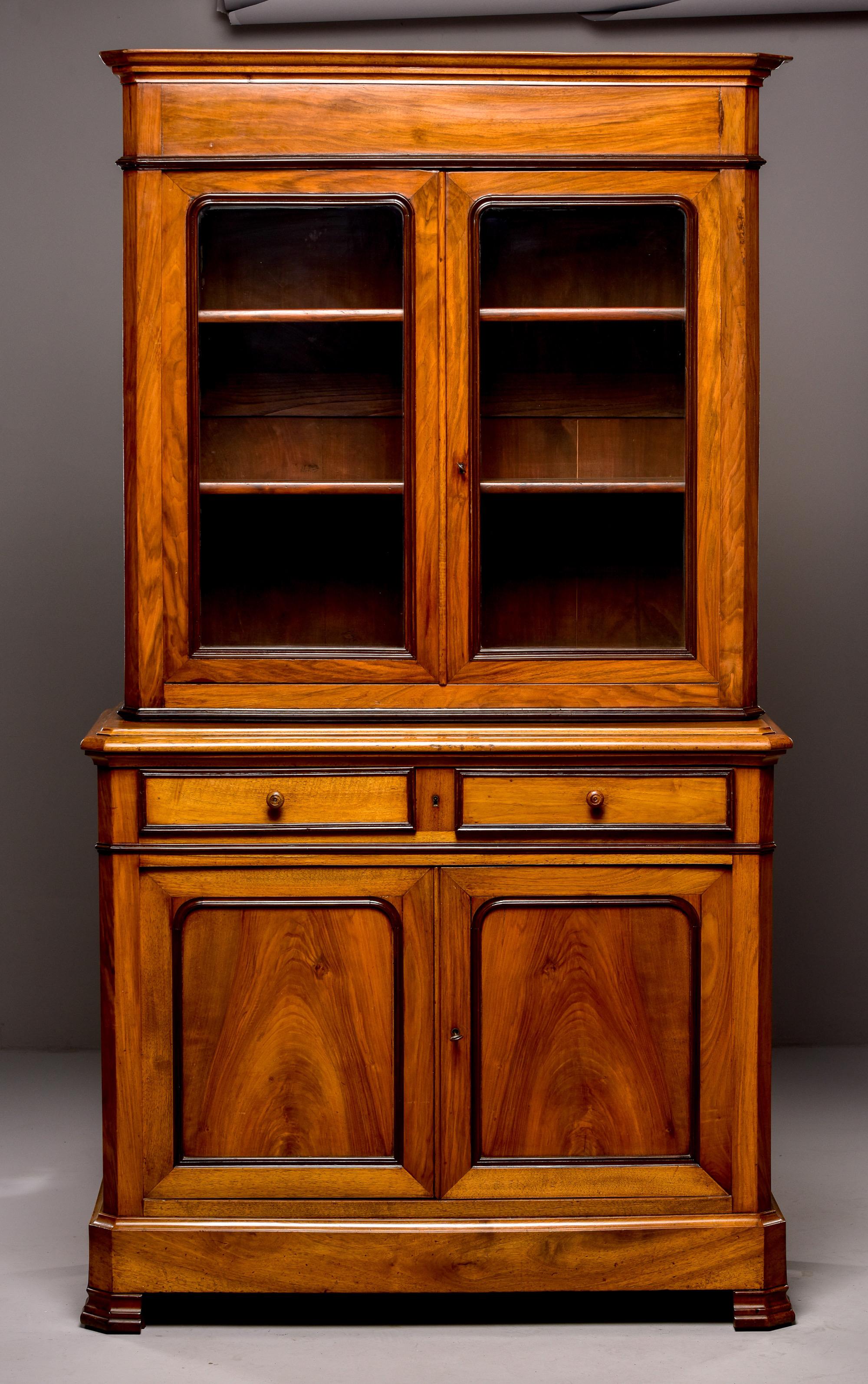 Circa 1880s French Louis Philippe mahogany buffet a deux corps. Features include a top section with locking glazed doors and two adjustable internal shelves, a footed base with two locking drawers over a locking compartment with a single adjustable