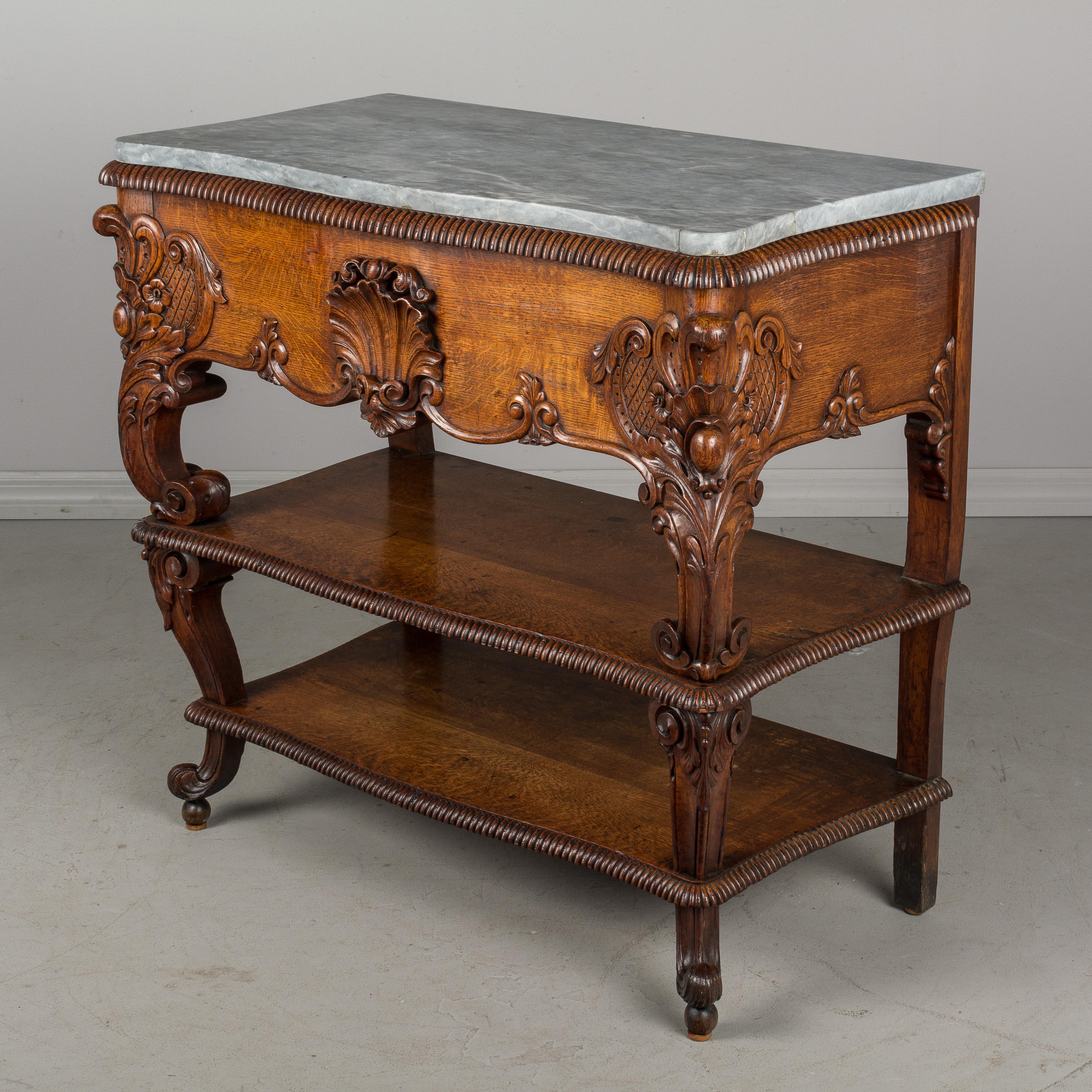 A 19th century Louis XV style console from Belgium made of solid oak with elaborate hand carved corner decoration and a large shell carving in the center. Two shelves spaced 7