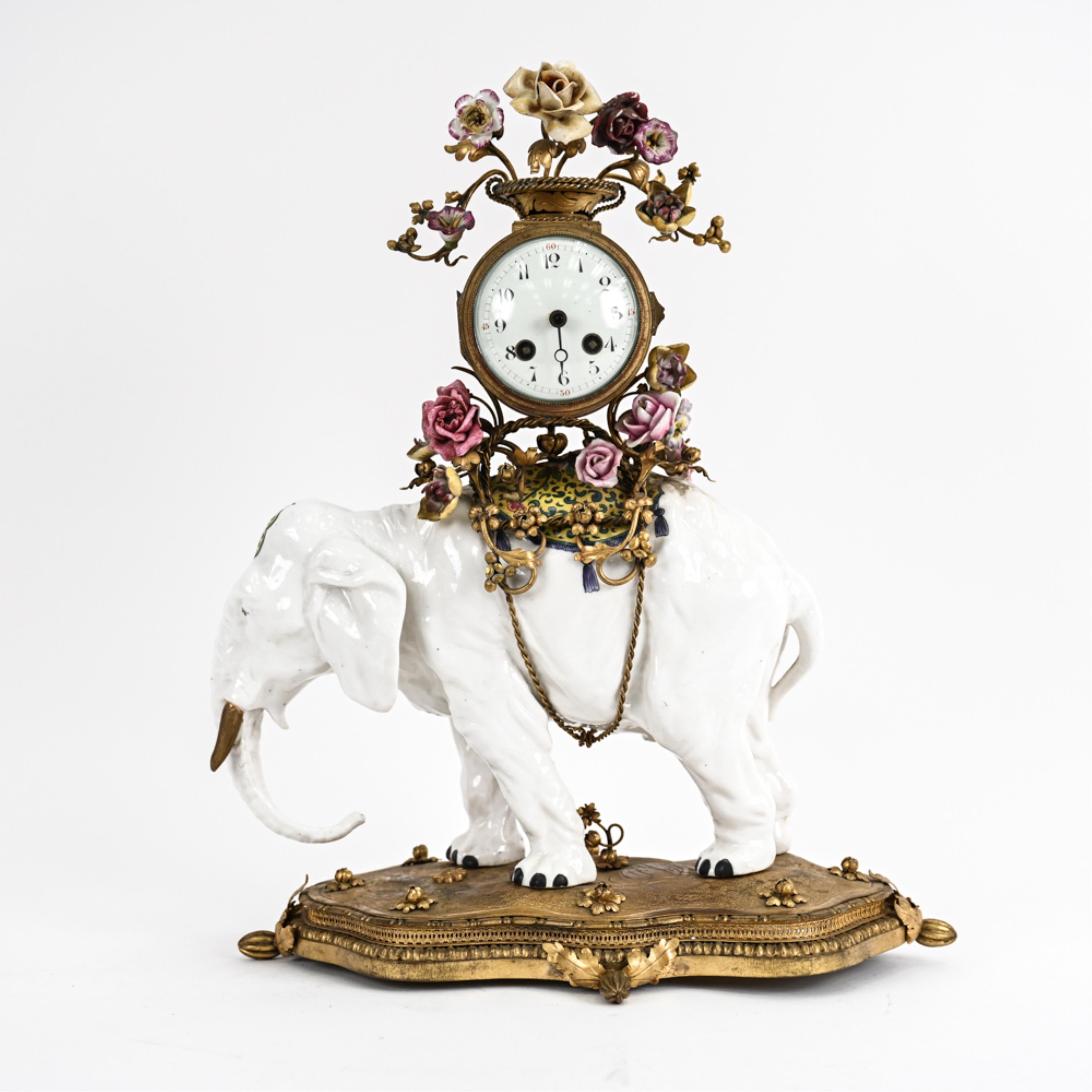 A fine Louis XV-style elephant mantle clock, featuring a porcelain Benjarong-style elephant with hand painted decoration and gilded tusks, mounted atop a naturalistic gilt bronze base and carrying a French drum-form clock adorned with porcelain and