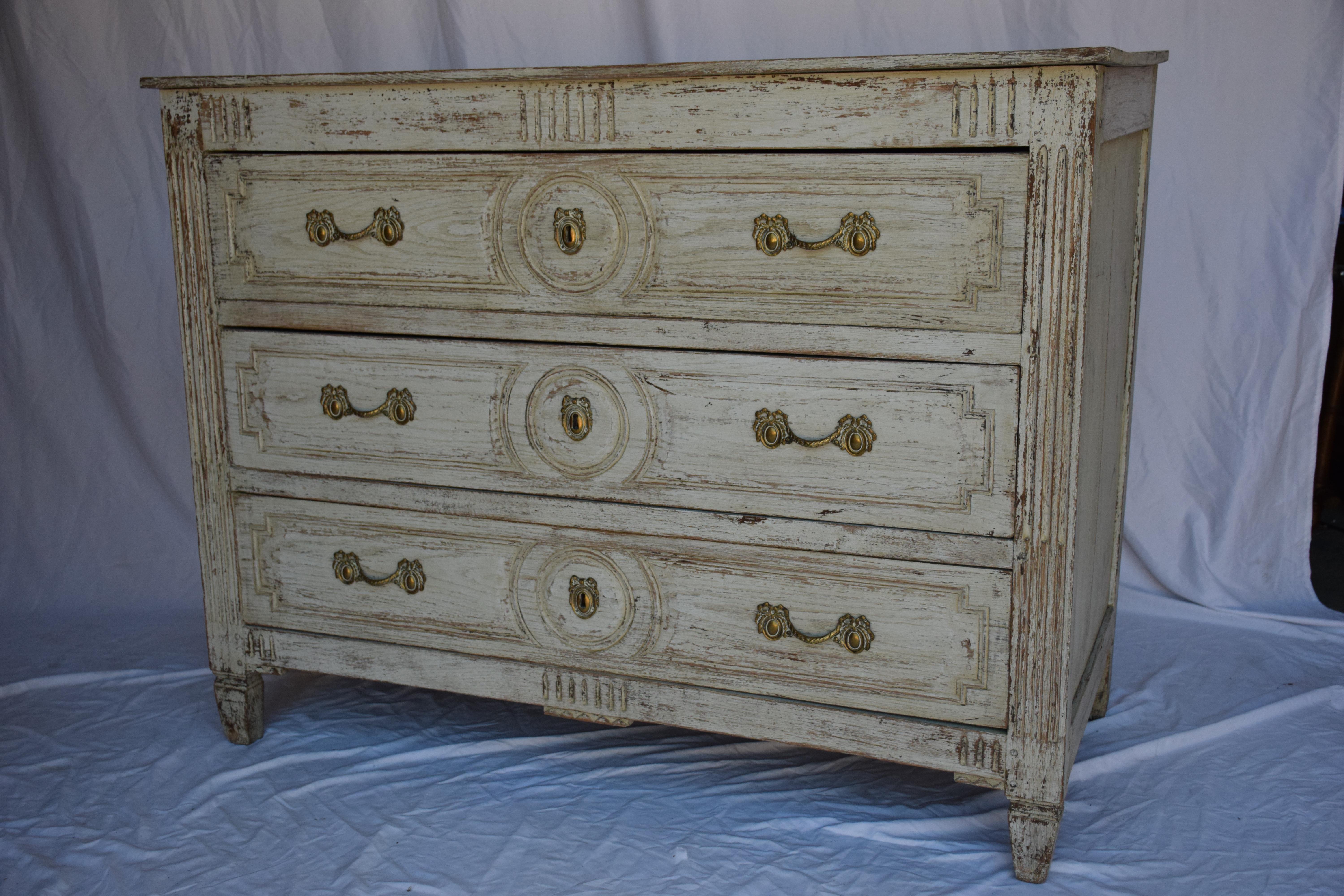  19th century French Louis XVI style commode features intricate carvings and a painted finish, adding a touch of antique elegance to any space. The piece exudes a regal charm with detailed craftsmanship and classic design elements. This commode