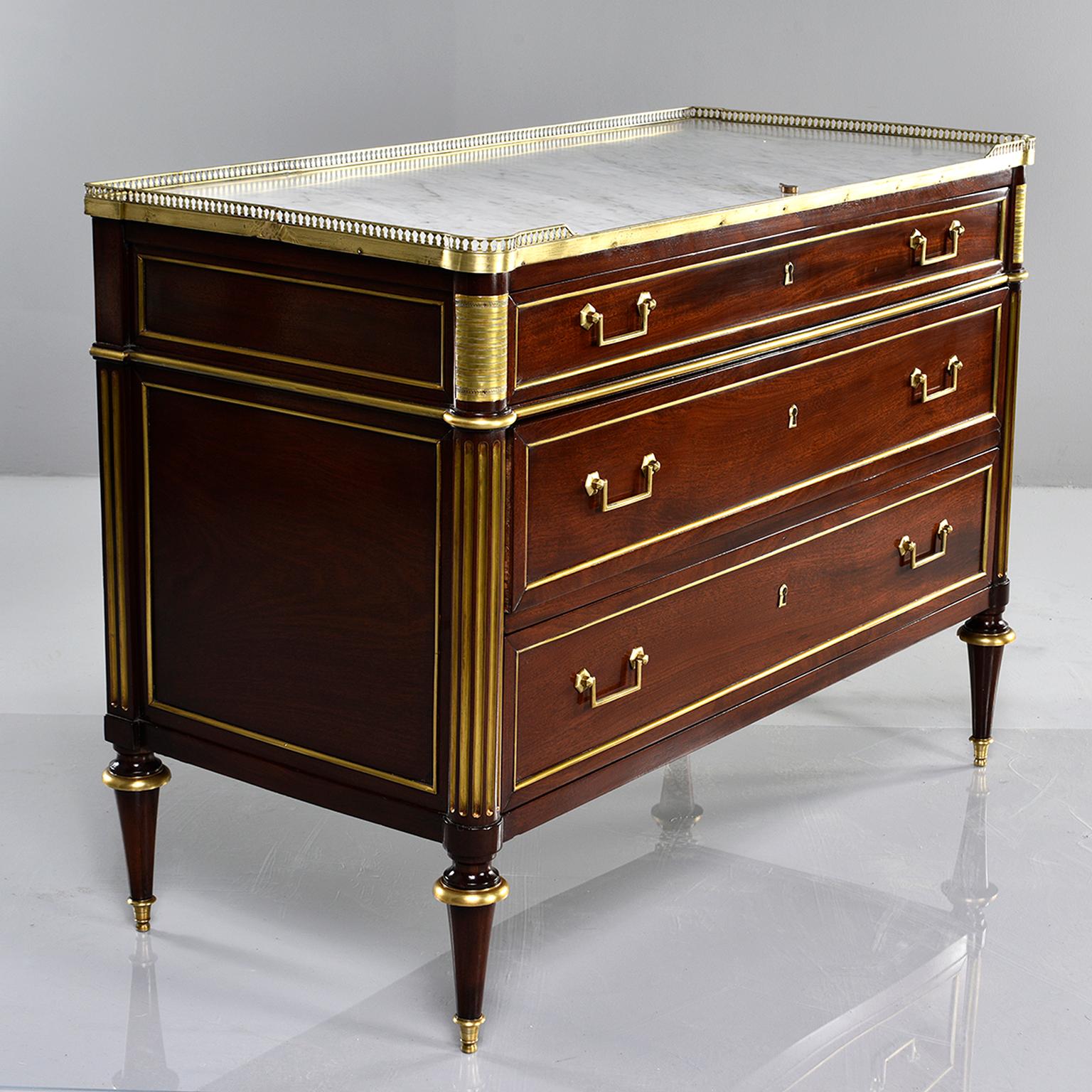 Three-drawer mahogany commode in Louis XVI style with brass trim and hardware, circa 1850s. White marble with gray veining on top with open work brass gallery. Three drawers with functional key lock. Reeded and gilded detail at side supports, brass