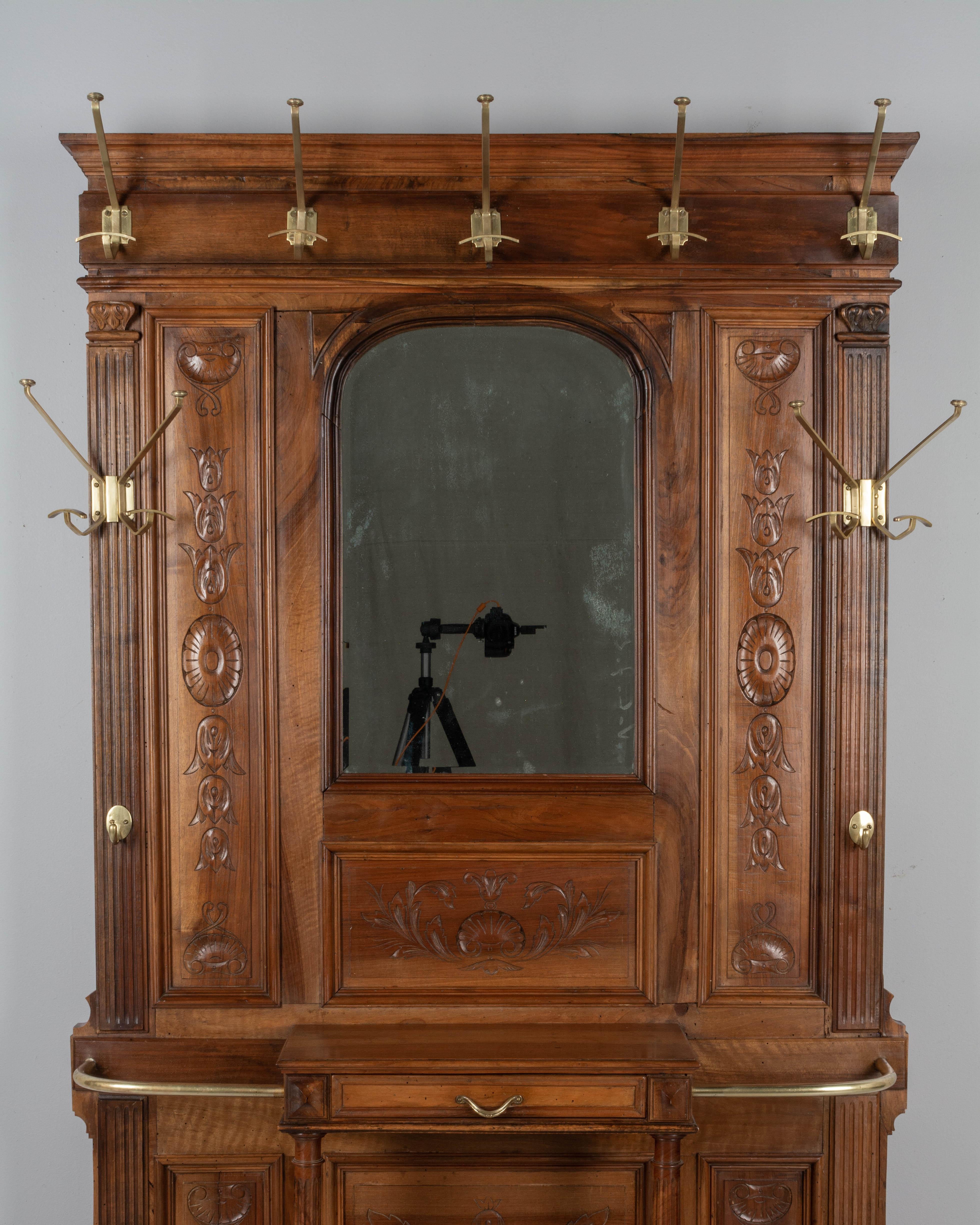 A Louis XVI style French entryway hall tree, or coat rack, with arched beveled mirror. Made of solid walnut with hand carved decorative panels and cast brass coat hooks. Dovetailed drawer for gloves in the center is supported by turned fluted