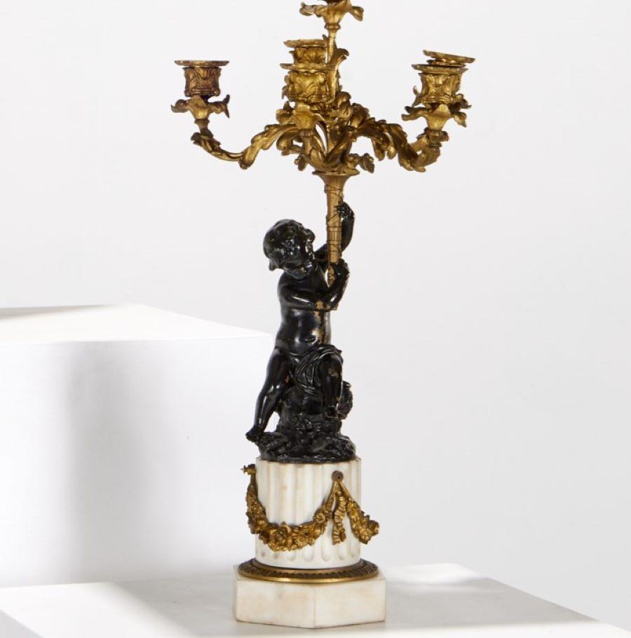 S. XIX, Francia, pareja de lámparas candelabro estilo Luis XVI de bronce patinado y dorado. Cada lámpara con un putto sentado portando una antorcha que emite un candelabro de 6 brazos foliados, todo ello montado sobre base de columna de mármol
