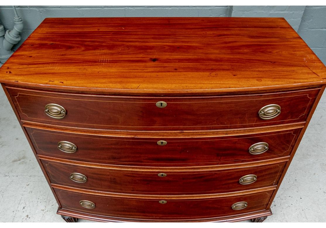 A Antique Bow front Chest with fine traditional form. Fine construction with four graduated long drawers with string inlays. Brass bales and keyholes (lacking a key). The carved skirt rail raised on ribbed, turned tapering legs on ball feet. 
W. 45
