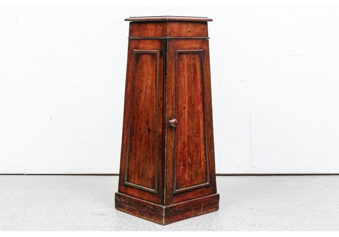 A square cabinet narrower at the top in the shape of an ancient Egyptian pylon. The top with a carved edge, the recessed sides and front door with carved moldings. The interior with two shelves. Suitable as a sculpture stand. 
Measures: H. 38