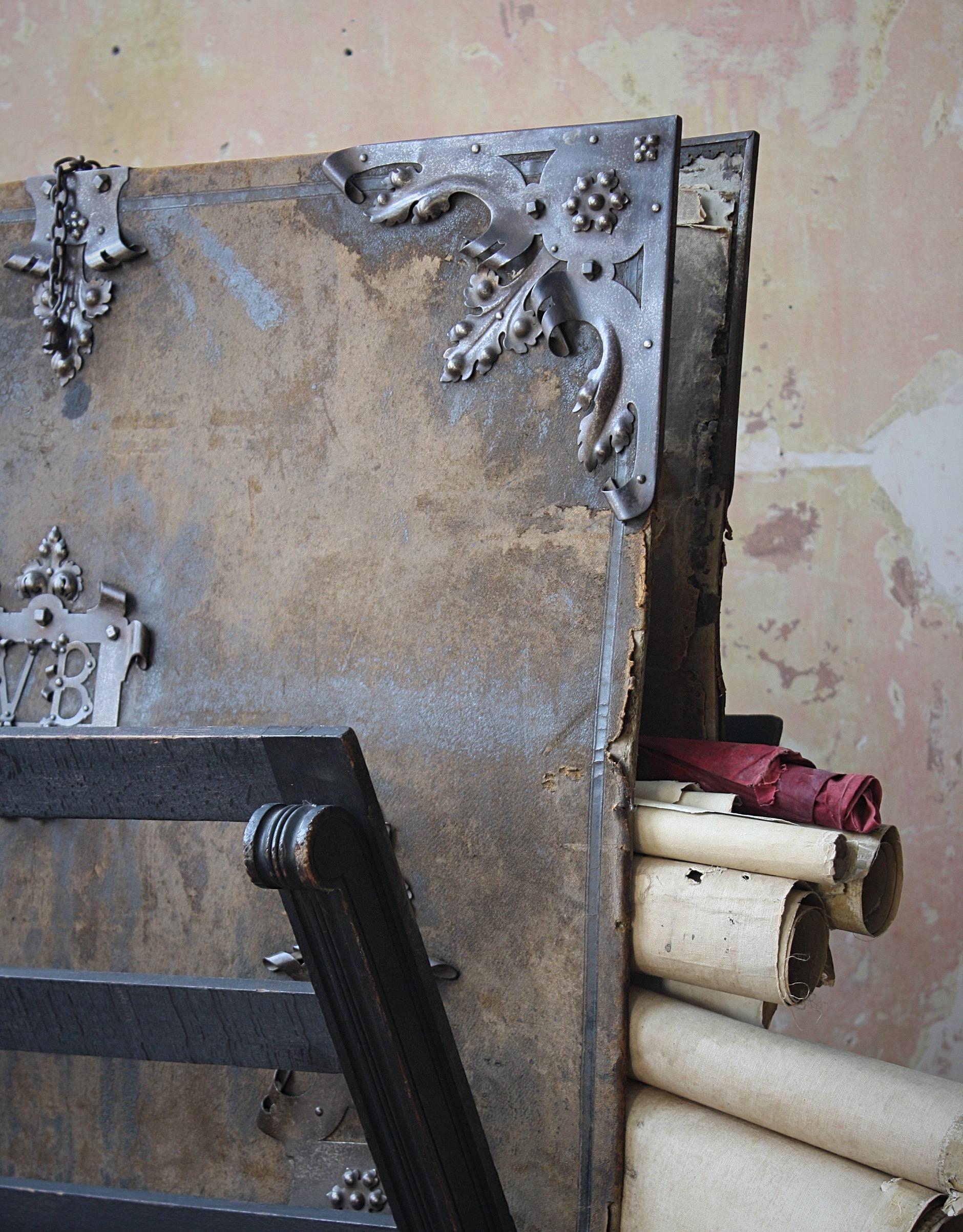 Un cavalletto e un faldone decorativi in stile gotico, il cavalletto in pino con finiture originali in ebano, il faldone rivestito in pelle verde perfettamente usurata con cartigli in acciaio, cinghie, targhetta centrale siglata con V.B. e una