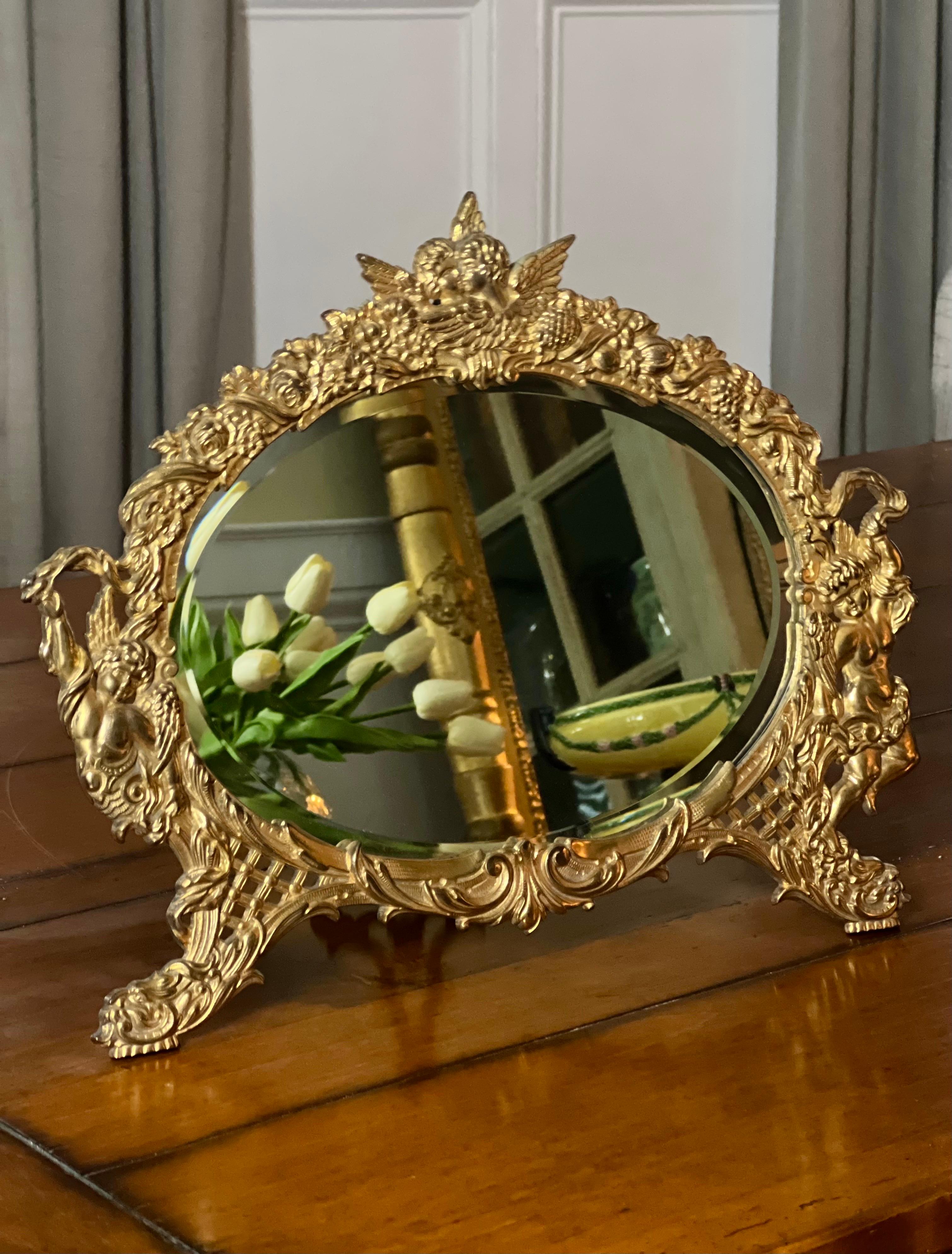 Miroir de table ovale elliptique biseauté en fonte dorée, de style chevalet, orné, par National Brass and Iron Works, fin du 19e siècle. Il présente un travail en relief complexe, percé et gravé, de chérubins entourés de fleurs d'un côté et d'une
