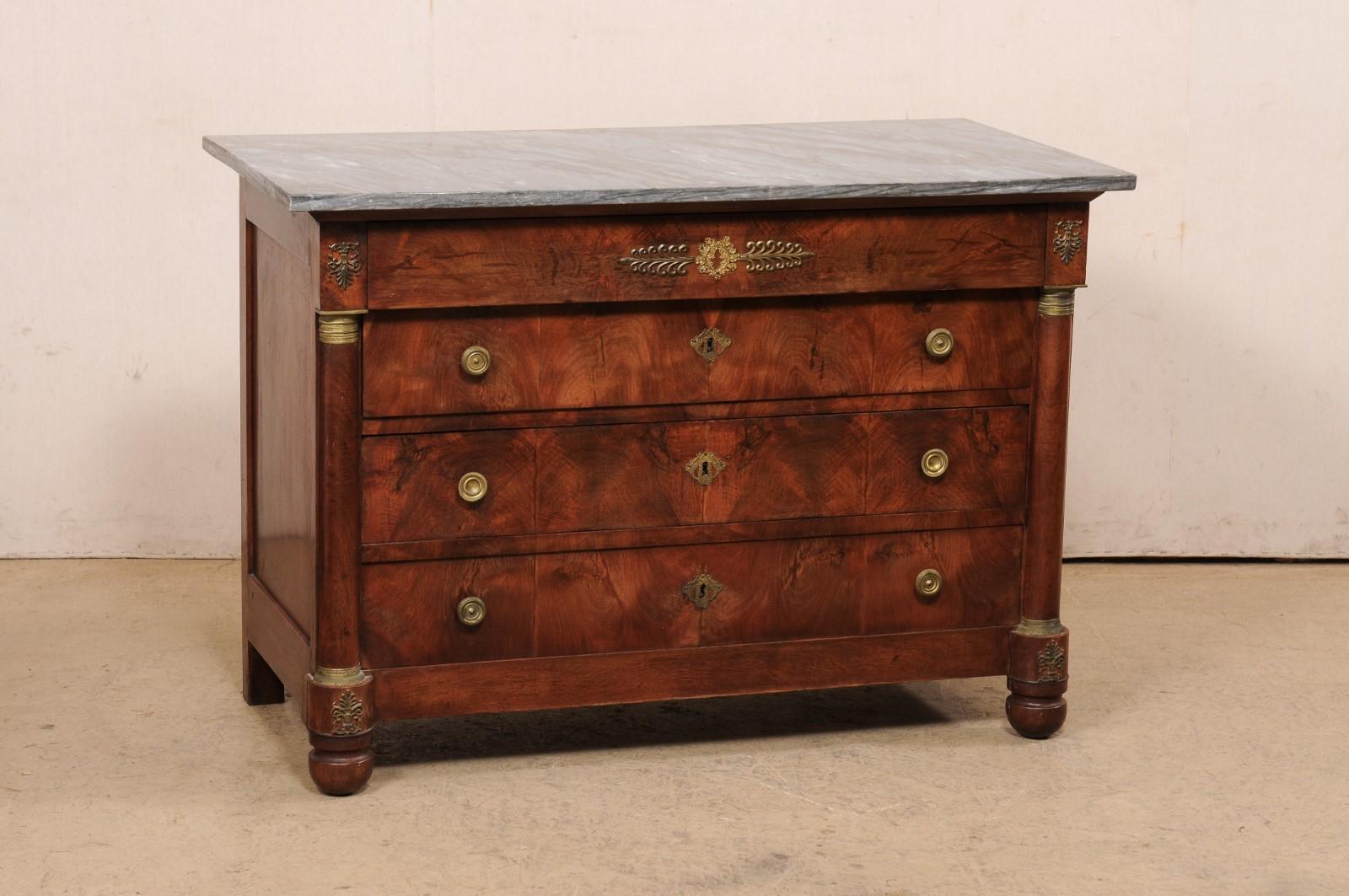 A French Neoclassical commode, with marble top and exquisite brass accents, from the 19th century. This antique chest from France features a rectangular-shaped gray marble top, over case which houses four drawers (upper drawer is disguised within