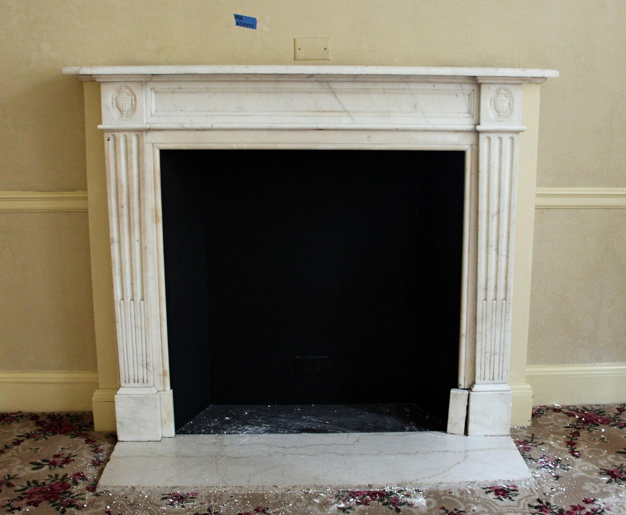 Hearth not included. This is a 19th century English Regency mantel hand carved from white Carrara marble with slight gray veining. Features hand carved urn detail on the top plinths. This mantel was one of a group of antique mantels imported from