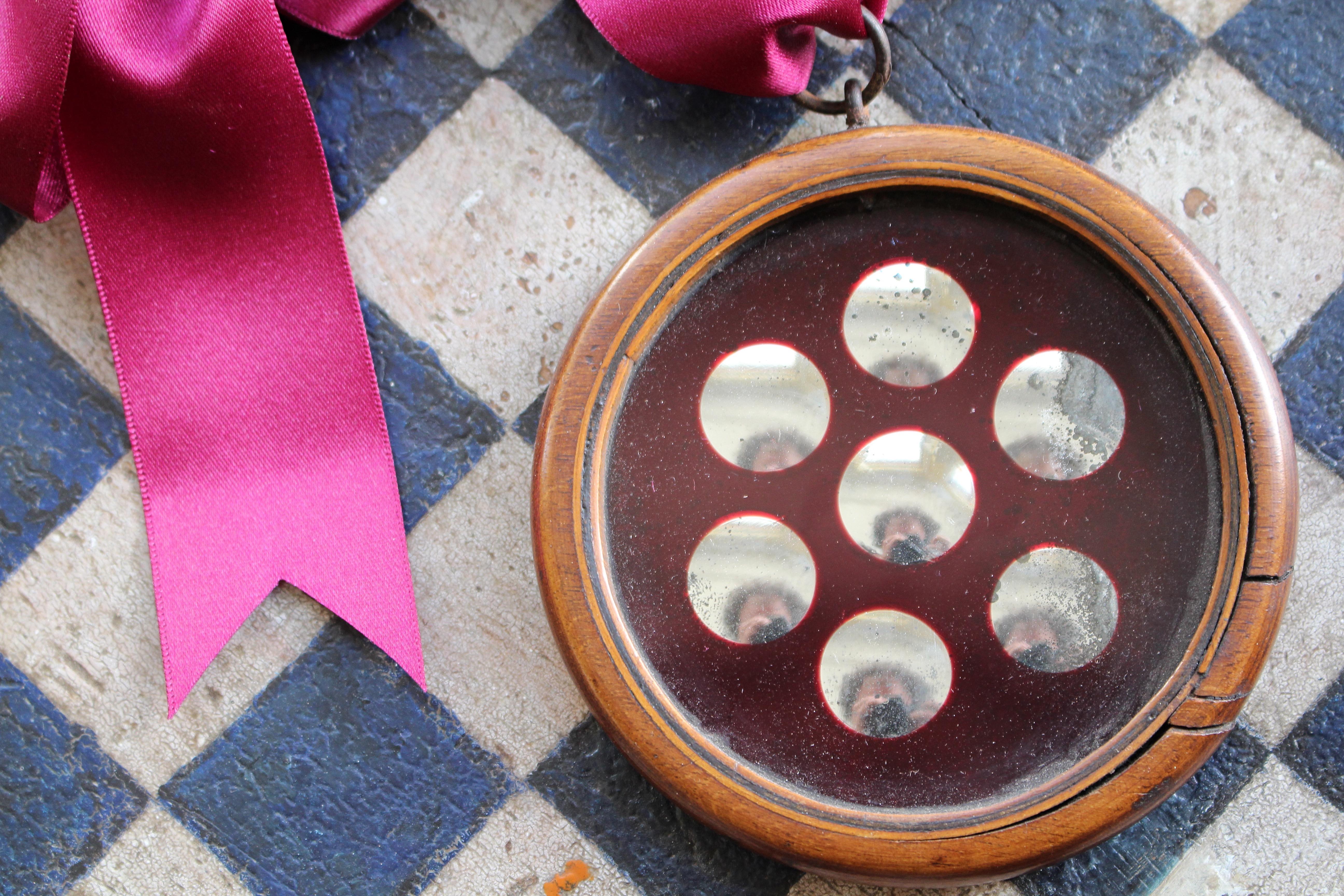 A decorative double sided sorcerers mirror, with seven reverse ground optics on a ruby red glass ground, with the other side being a flat plate.

The mirror plates have age related oxidizing and pitting.

The ribbon has been added for decoration and