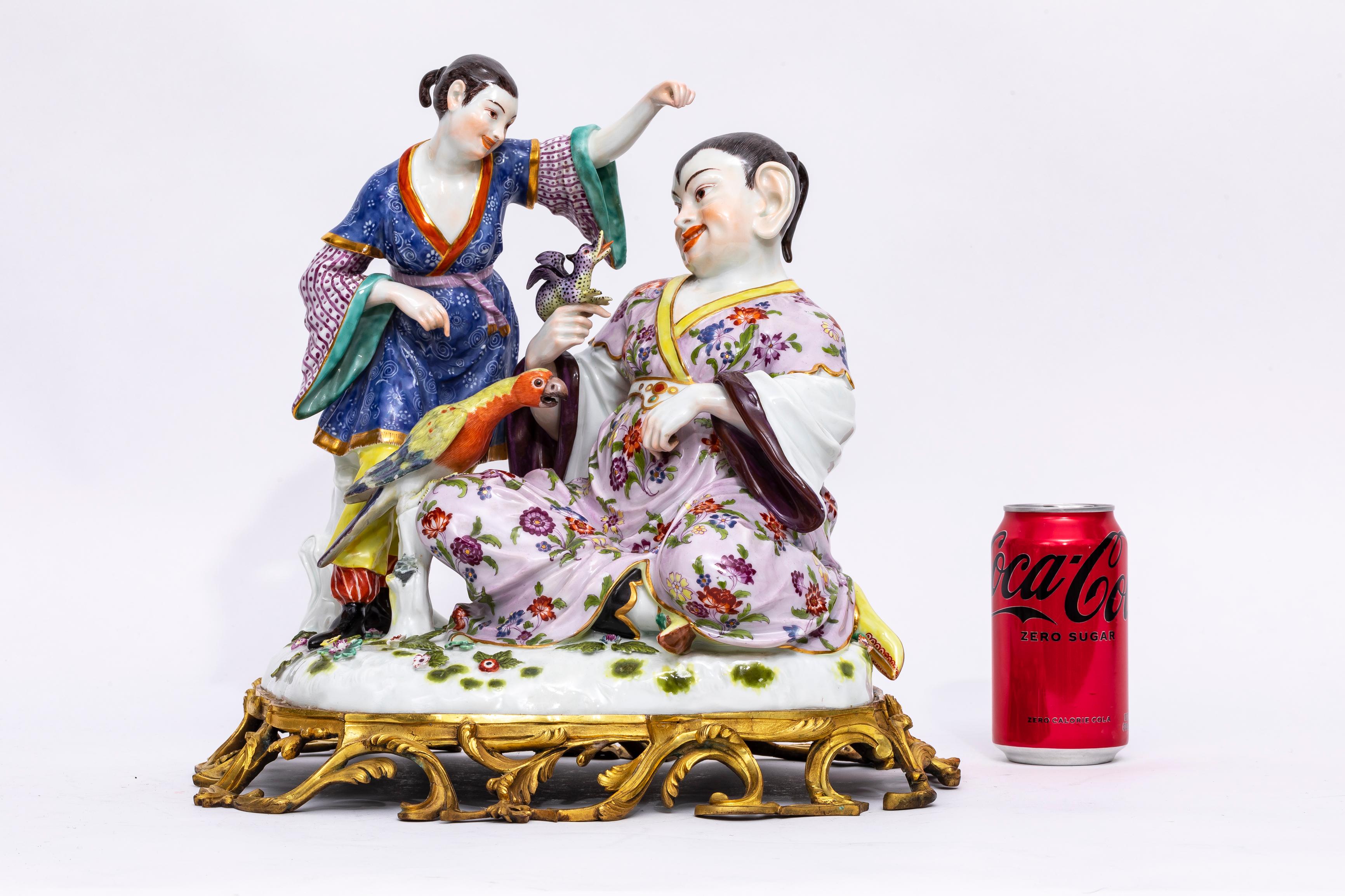 A Large and Quite Unusual 19th Century Ormolu Mounted Meissen Porcelain Chinoiserie Group with Parrot and Dragon.  The sculpture features many floral motifs and decorations. Robes worn by the two figures are patterned with delicate flowers—small