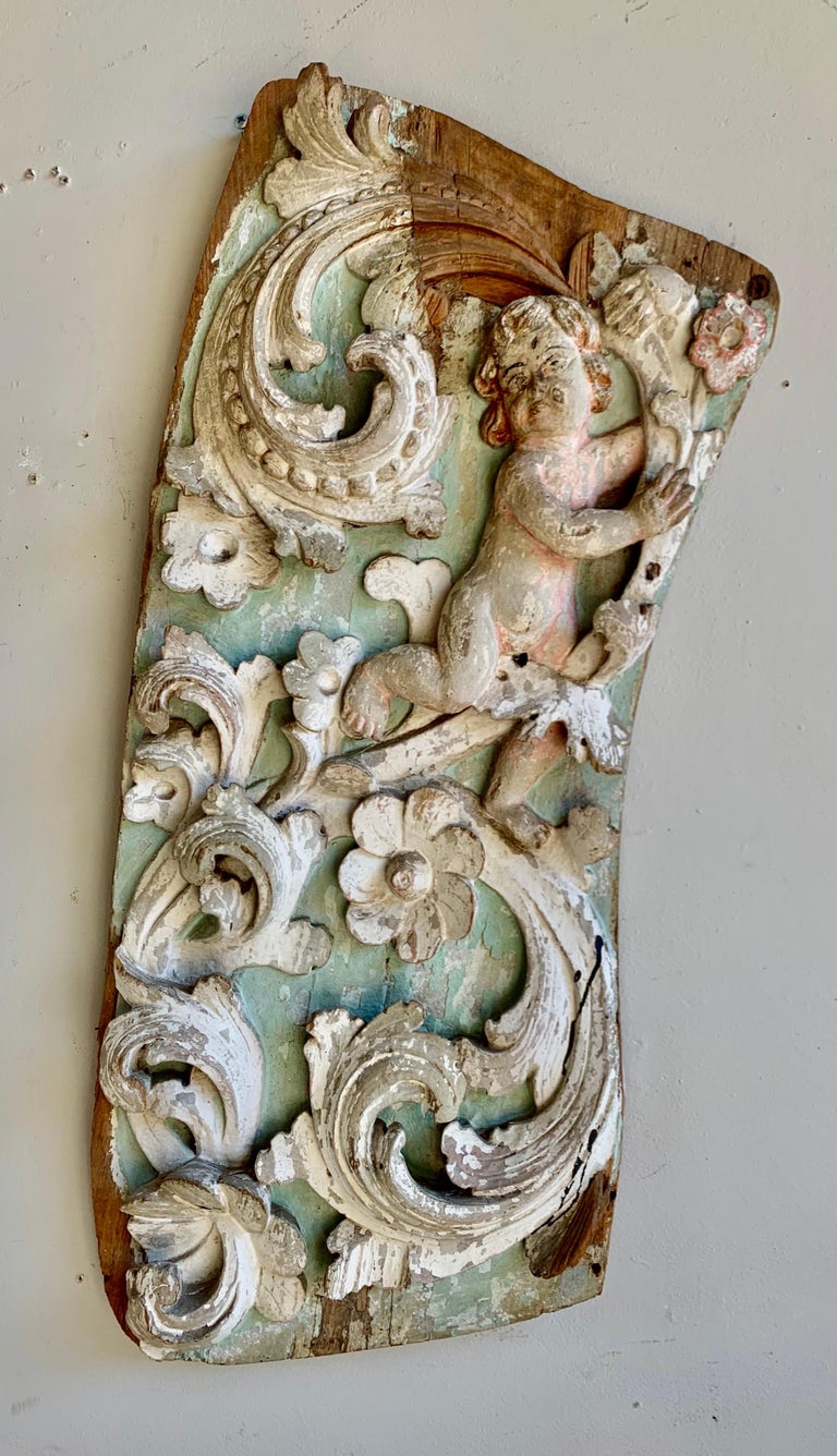 19th century painted Italian carving depicting cherubs, flowers and swirling acanthus leaves. The panel is painted in soft shades of robin's egg blue and cream with natural colored wood showing under the paint.