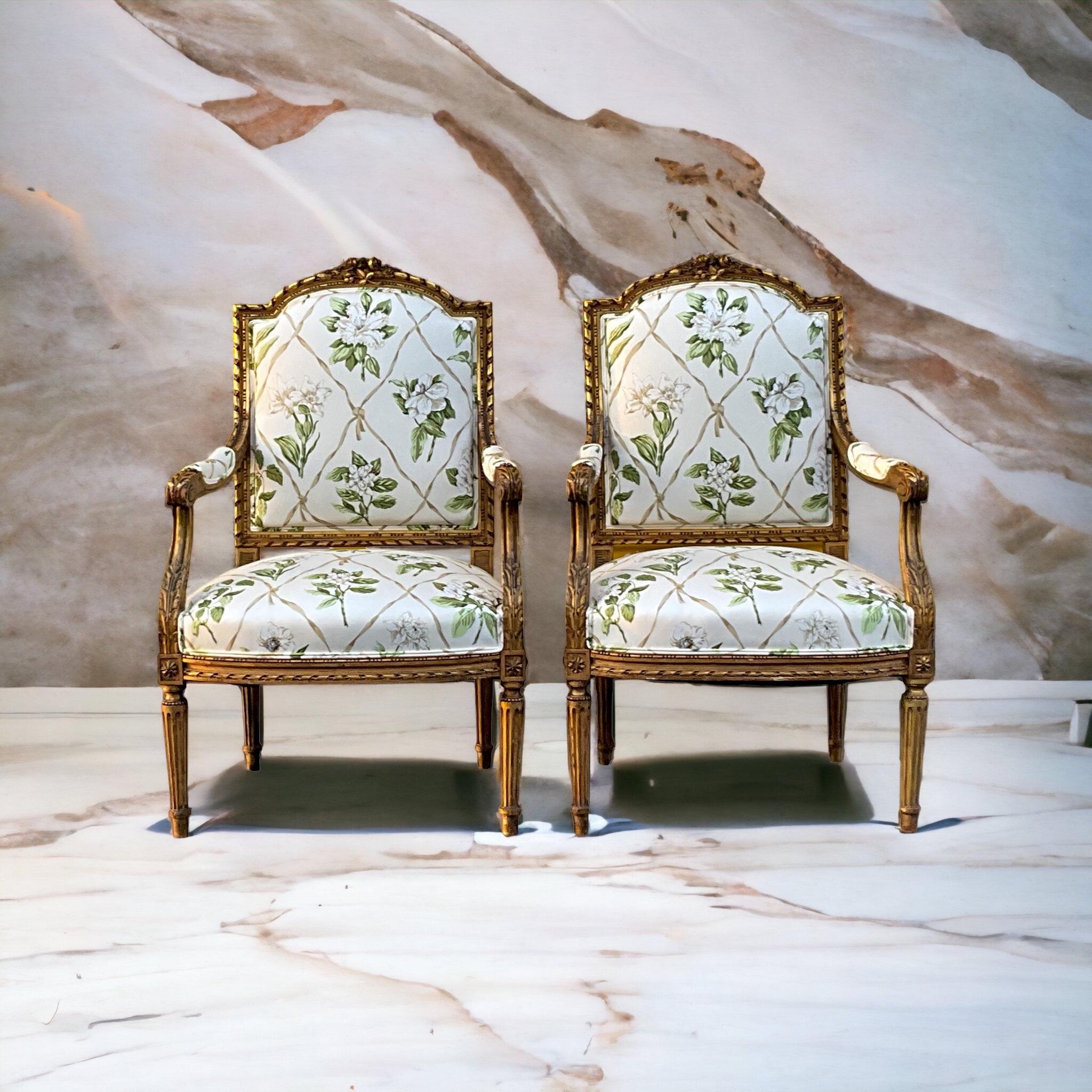 This is a pair of French Louis XVI style carved gilt wood bergere chairs in new upholstery. The upholstery is a lovely floral and ribbon cotton that I believe is by Travers.. The giltwood frames show some age appropriate wear but are sound. The arms