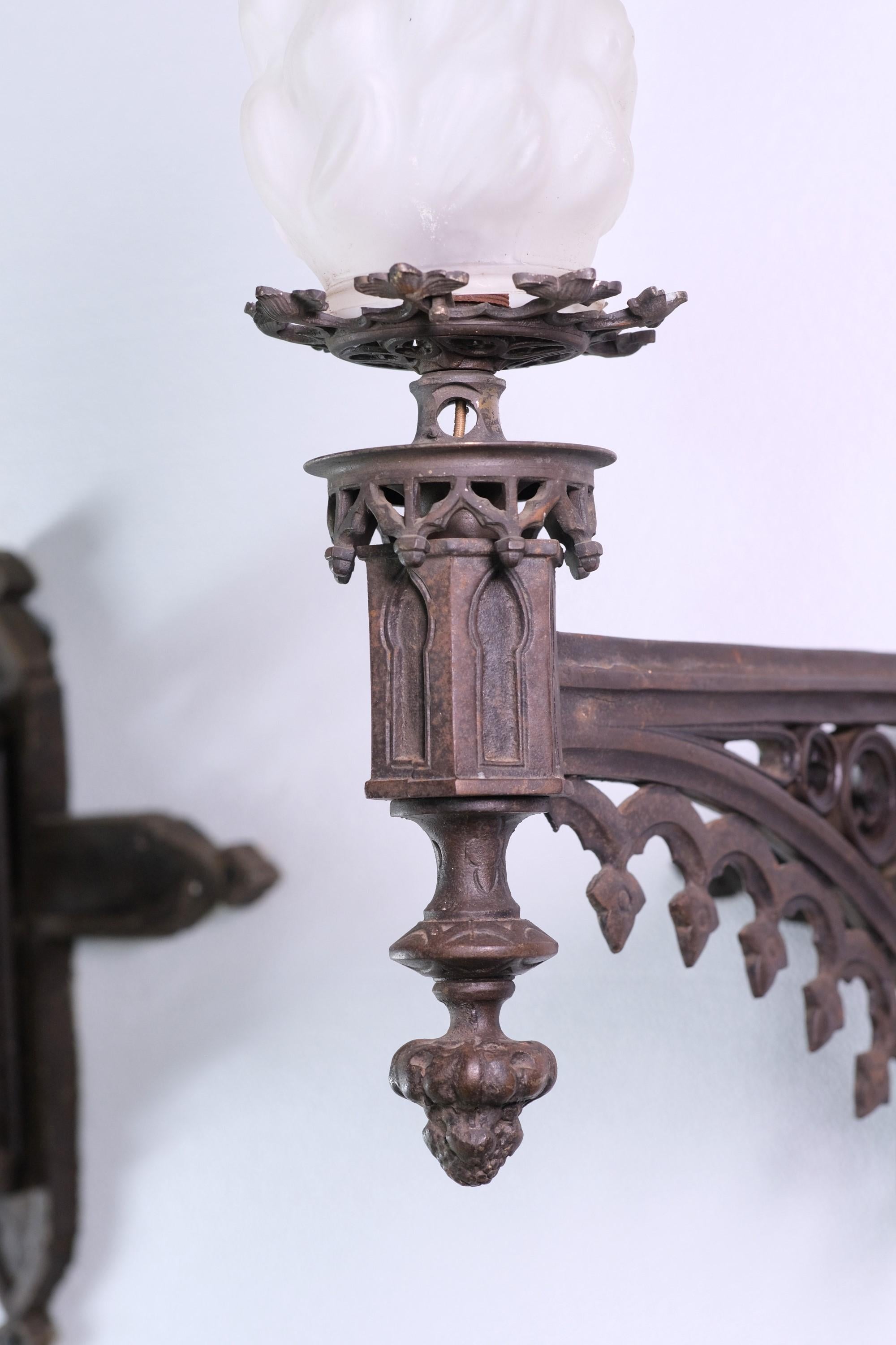 Antikes Paar gotischer Wandleuchter aus Gusseisen mit Flammenschirmen aus Milchglas. Die Arme der Leuchte sind an einer Kreuzhalterung befestigt und sehr detailliert. Gereinigt und neu verkabelt. Zum Zeitpunkt der Veröffentlichung ist eine kleine
