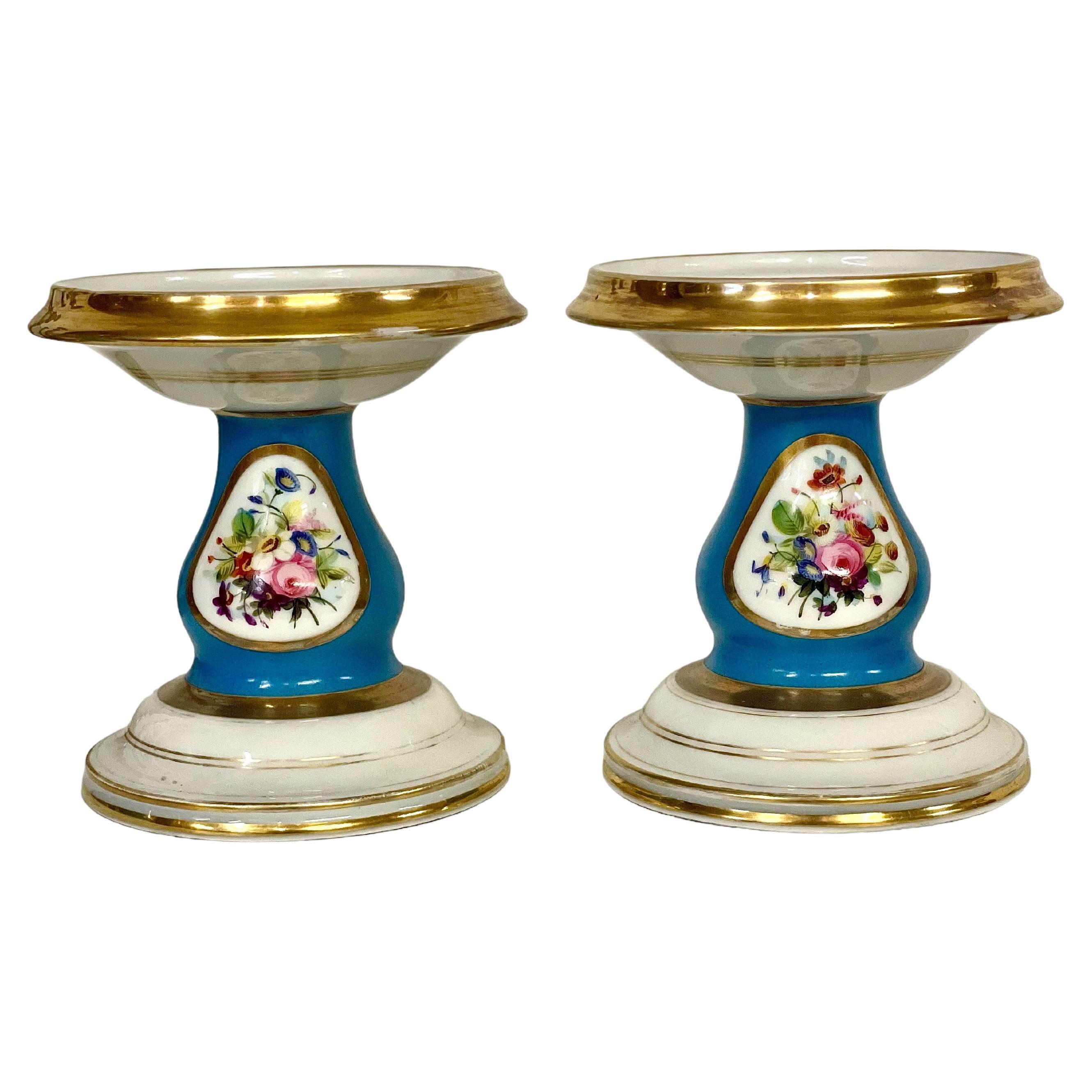 An exquisite pair of Porcelain de Paris 'cassolettes', finely crafted and hand-painted with a cartouche of polychrome flowers on a striking lapis blue background, ornamented all around with gilt accents. Each basin-shaped dish features its own