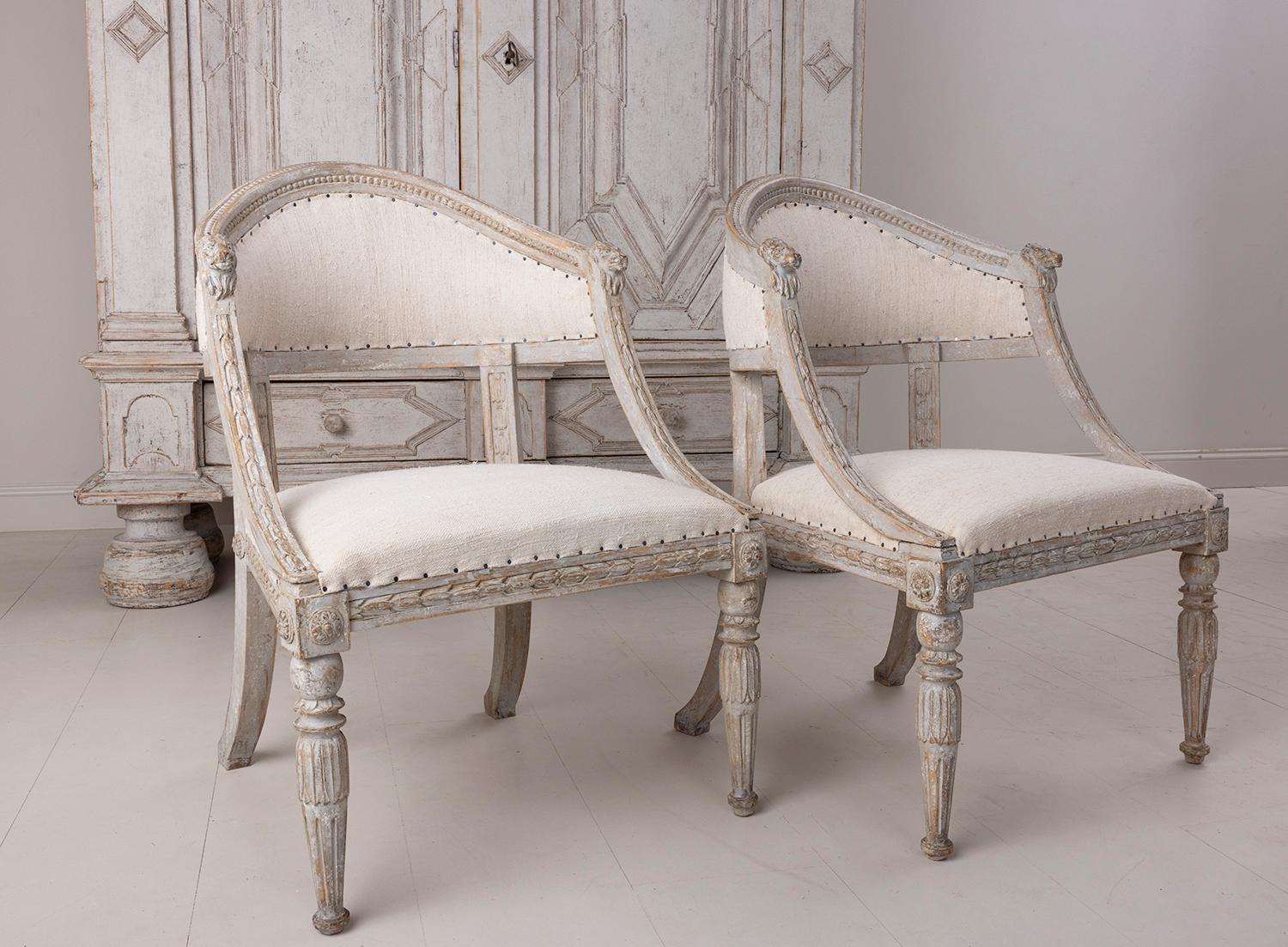 A Swedish late Gustavian pair of antique barrel back armchairs. These stunning chairs have shaped barrel backs with lion head carvings.  The frame features carved bell flowers with front legs adorned with lotus flowers and rosettes. This pair has