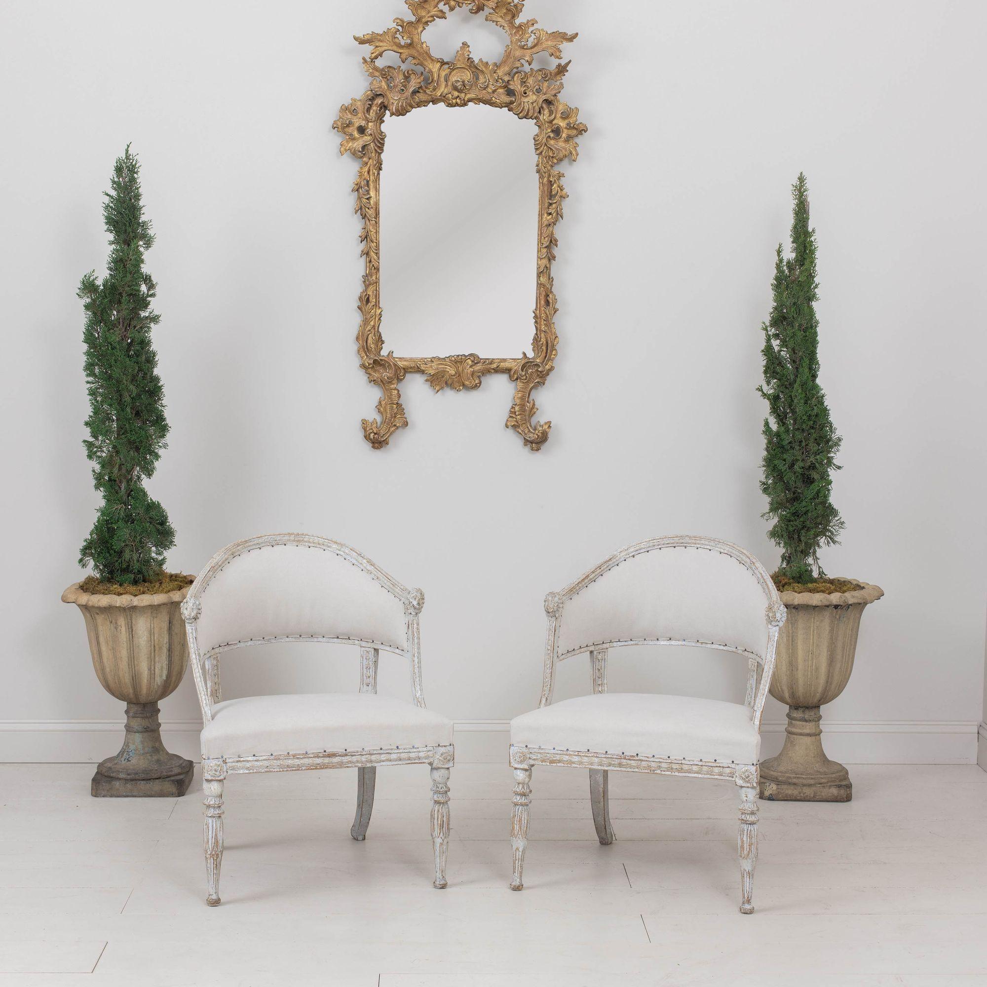 Paire de fauteuils suédois anciens à dossier en tonneau de la période gustavienne, vers 1810. Ces superbes chaises ont un dossier en forme de tonneau avec des sculptures en forme de tête de lion. Le cadre présente des fleurs en cloche sculptées et