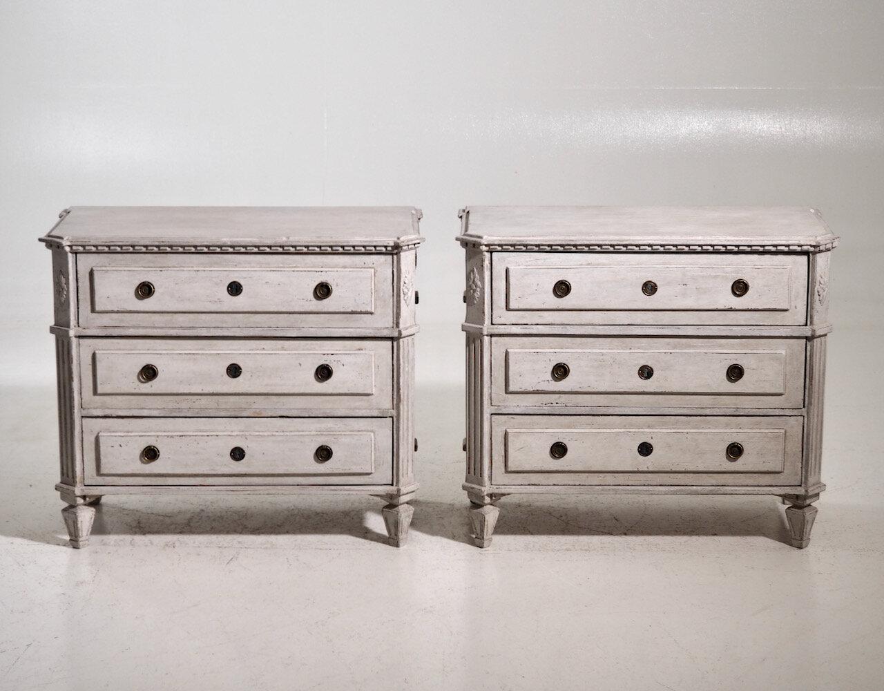 A special, neoclassical pair of Swedish Gustavian style painted chests with a soft gray patina. Each chest has dentil modeling around the top and three raised panel drawers with tapered legs. The corner posts are canted and fluted with carved