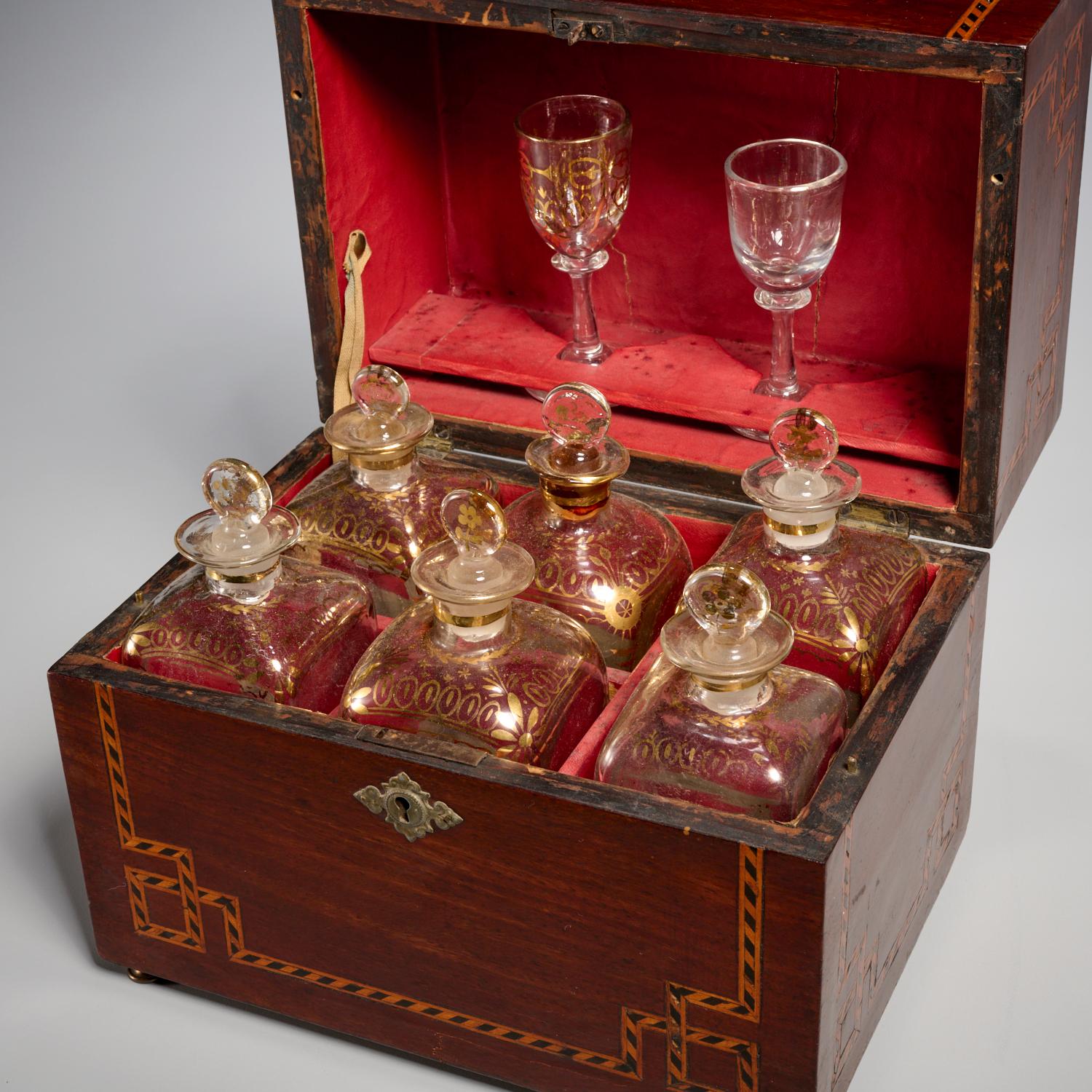 Mediados del siglo XIX, Austria, cueva de licor. Un estuche de chapa de caoba con incrustaciones de borde de cuerda de madera mixta, que se abre a un estuche con interior forrado de tela roja. El estuche contiene seis decantadores decorados en