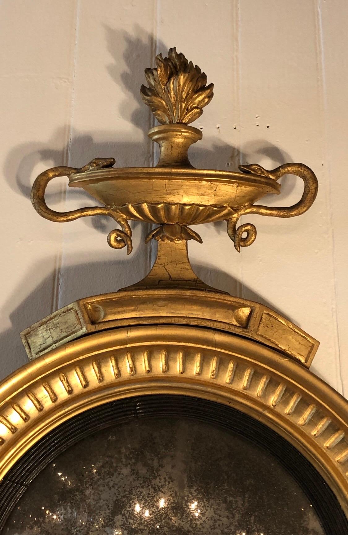 This exquisite English Regency girandole mirror has a classical double handle snake urn with flames. This British mirror has fluting and an ebonized reeded wood ring framing the convex mirror. The bottom has girandole arms flanking oak leaves. The