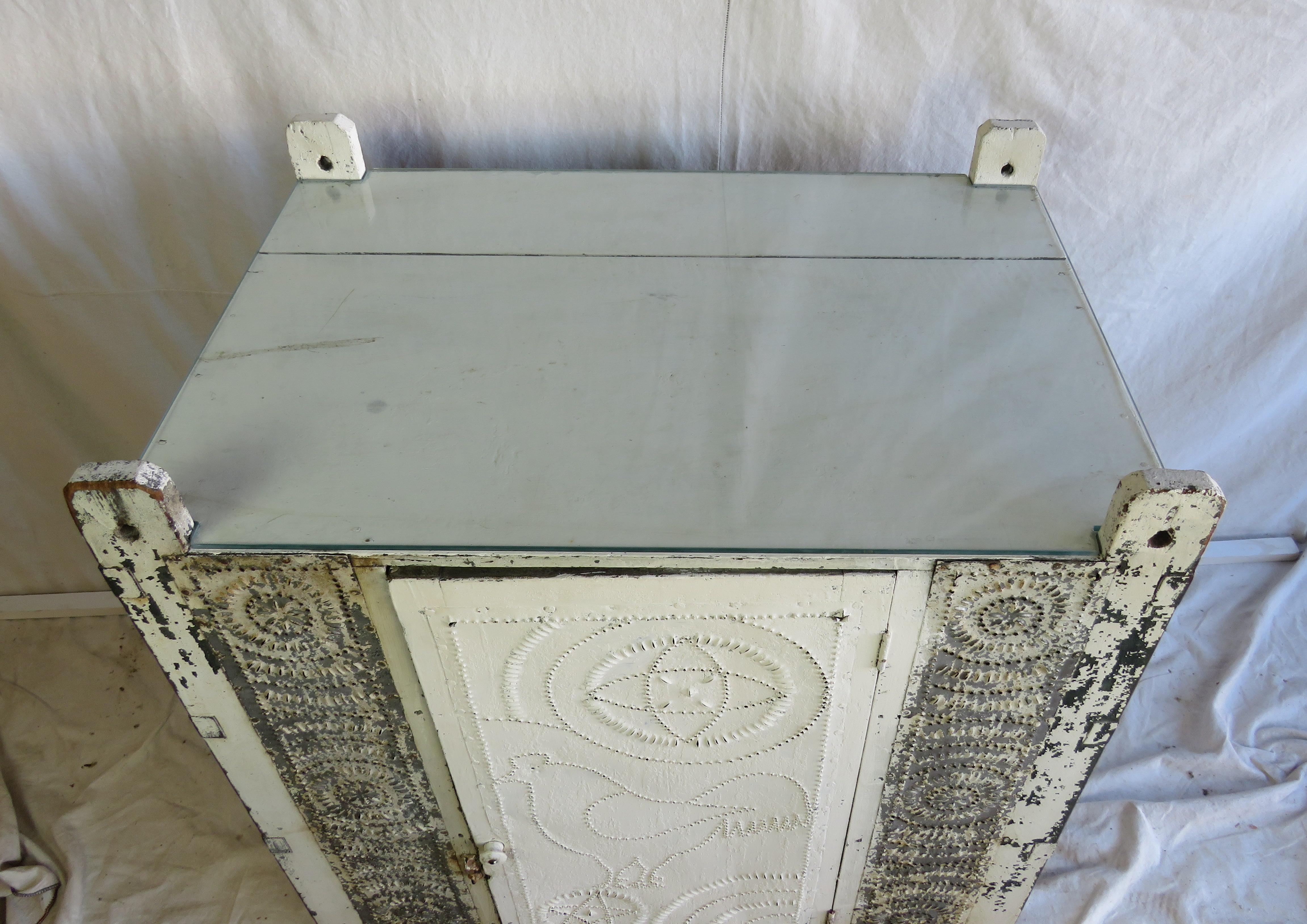 Diminutive 19th century pie safe cupboard in old white with punched tin details throughout. Decorations include a chicken, stars, rosettes, and pinwheels. Later notched glass top.