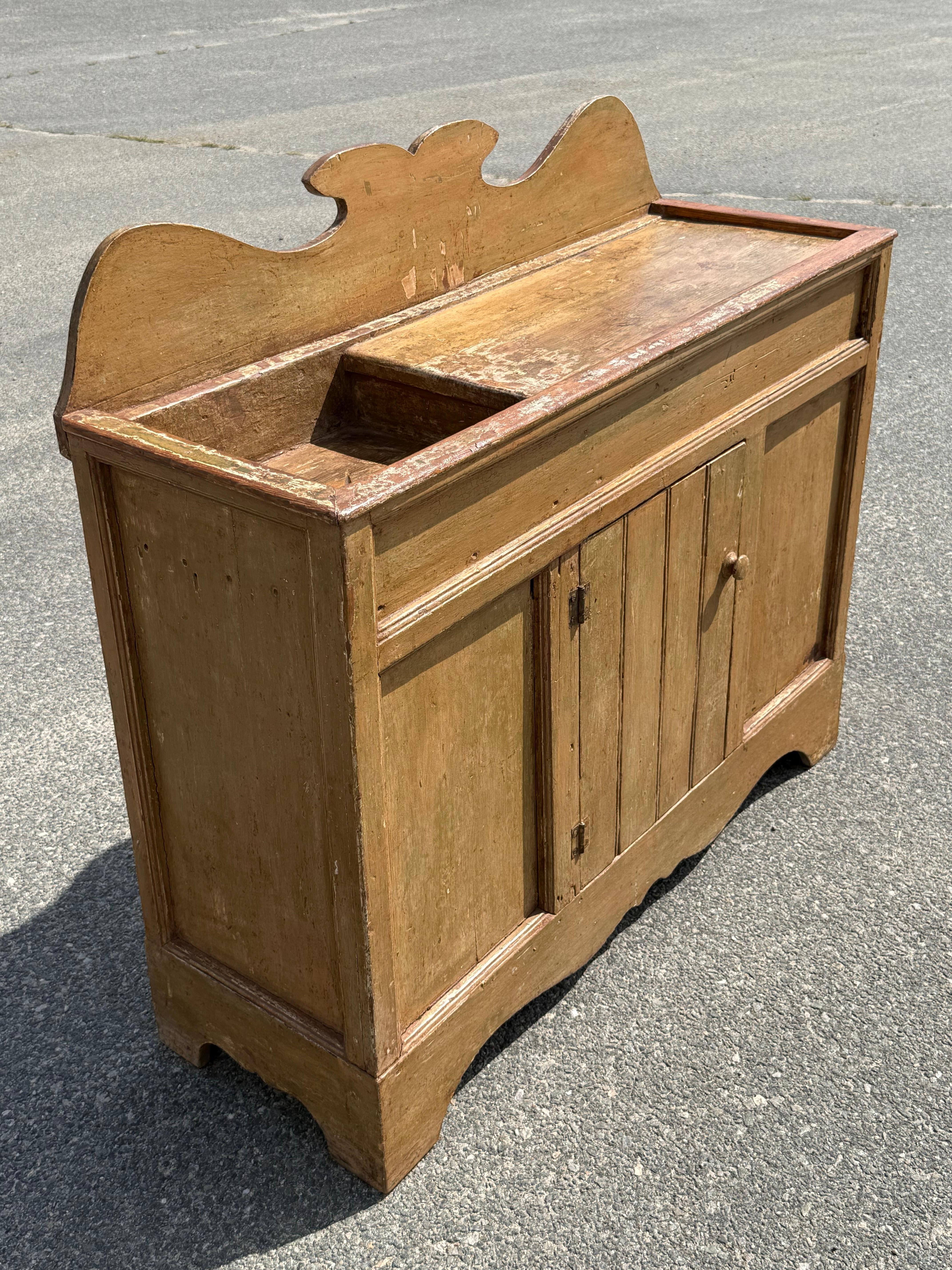 19th century pine dry sink in original ochre over green and red paints.  Shaped backsplash and star carved drain.  Single cabinet door reveals open interior.  Surface height 33.25 inches.