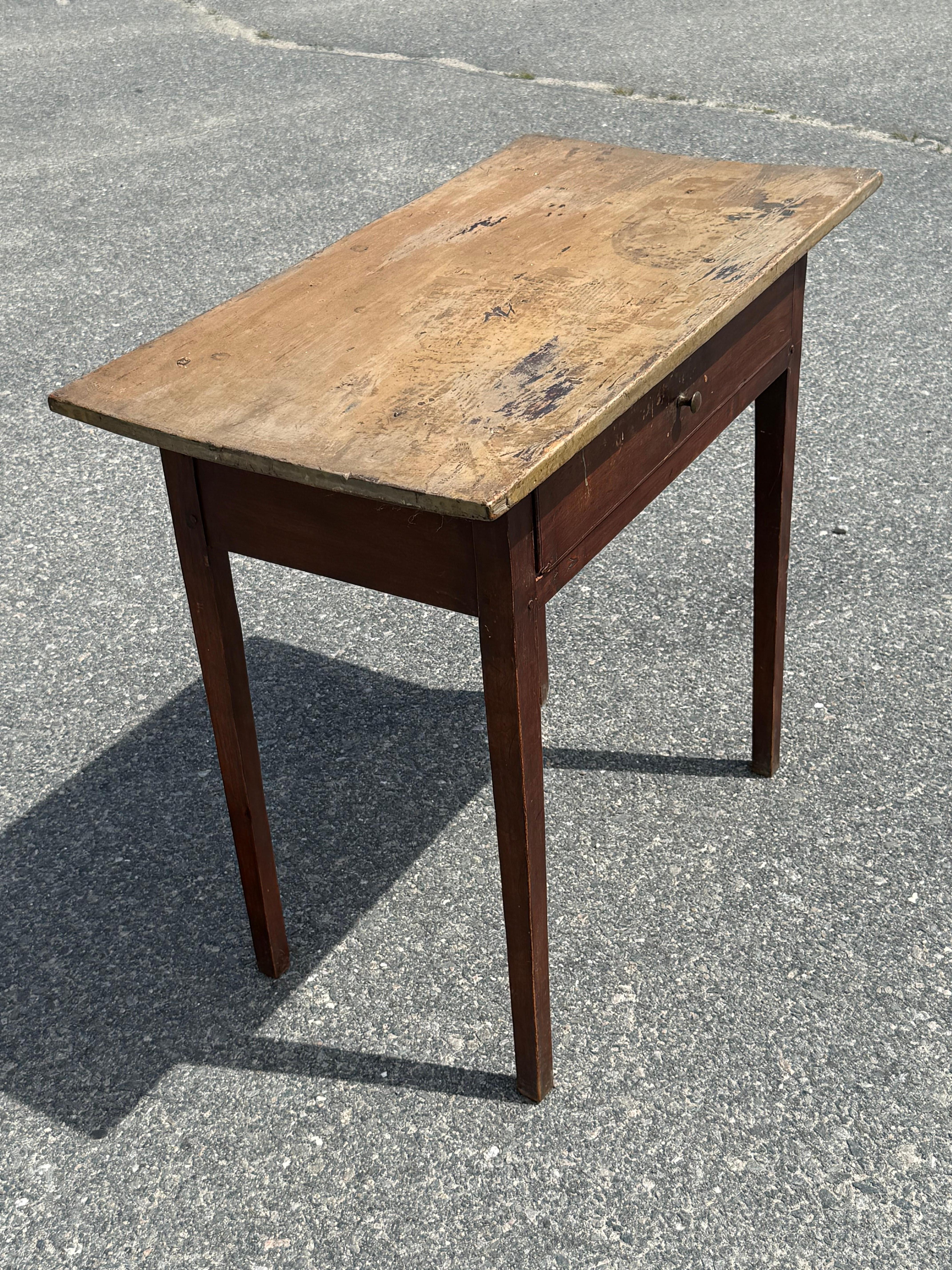 19th century pine one drawer stand in original paints.  Light color single board top with marks from age and use and some traces of old newspaper print from transfer at some point.  Dark brown base with single drawer with brass pull, on taper legs,
