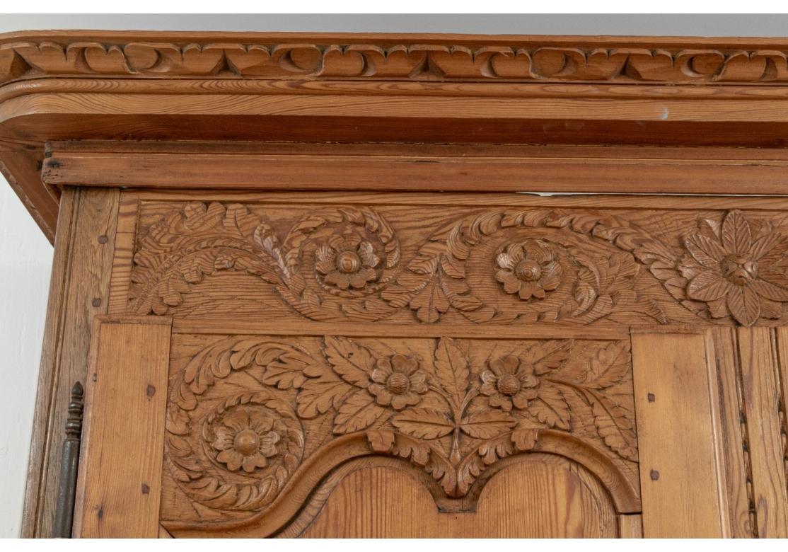 A two- part cabinet with carved cornice band. A carved foliate frieze over carved recessed doors with matching foilate upper panels. The lower carved foliate panels also with birds perched on wreaths. With classic curved French metal escutcheons.