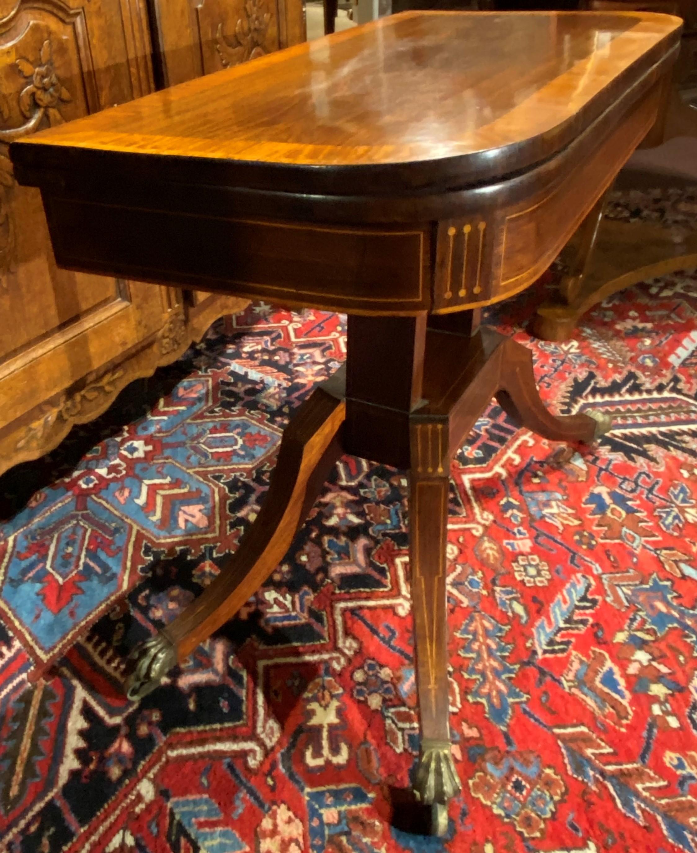 A nicely carved Regency gaming table in rosewood, with a contrasting inlaid top border, opening to a lavender or purple baize lining the interior top, with a storage compartment underneath, all supported by two rectangular pedestals with line inlay