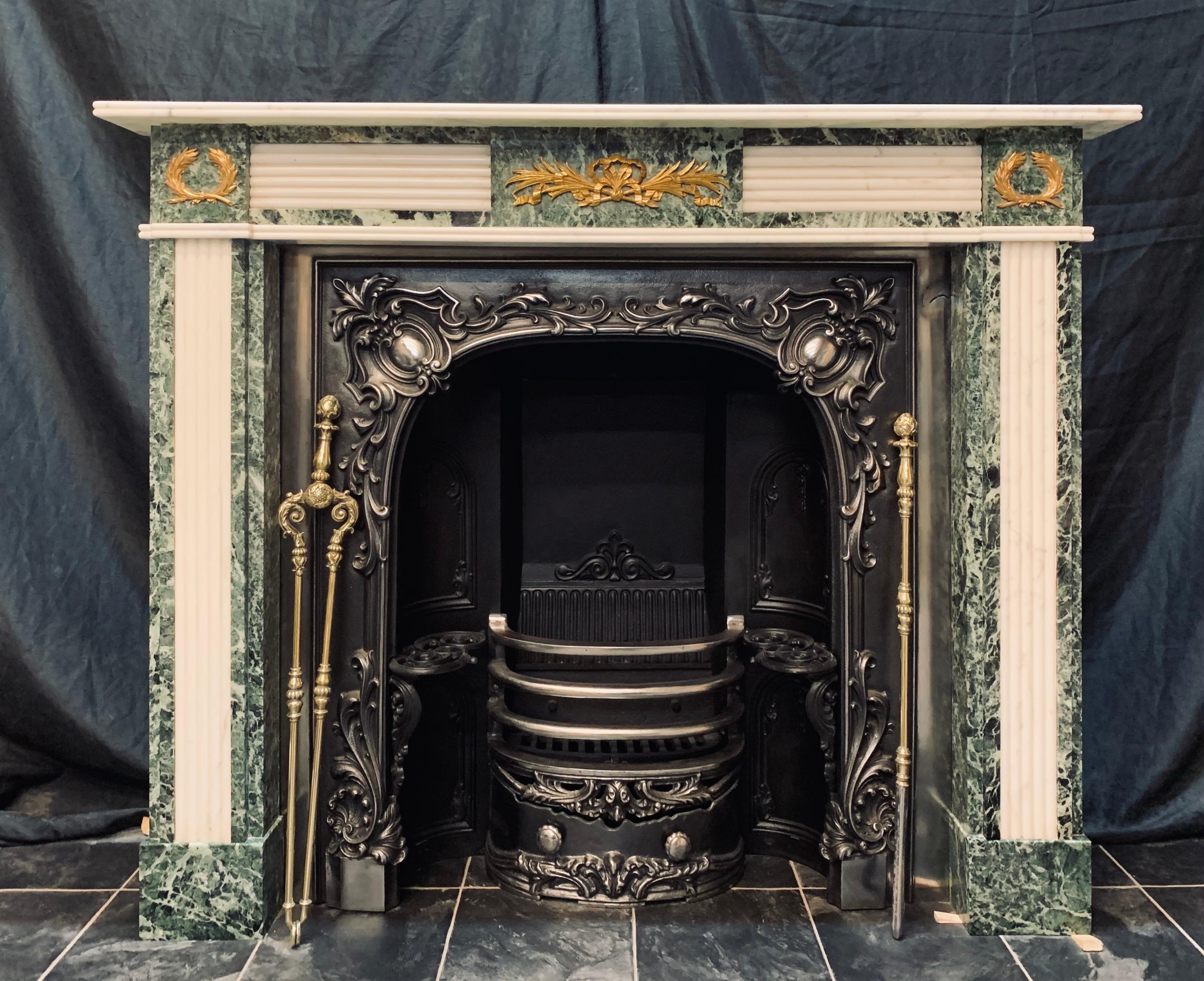 An elegant and detailed Regency style richly veined Verde Tinos & Statuary marble fireplace surround with bronze ormolu mounts. A reeded top shelf sits above a frieze hosting a central tablet with a symmetrical bronze ormolu mount, flanked by