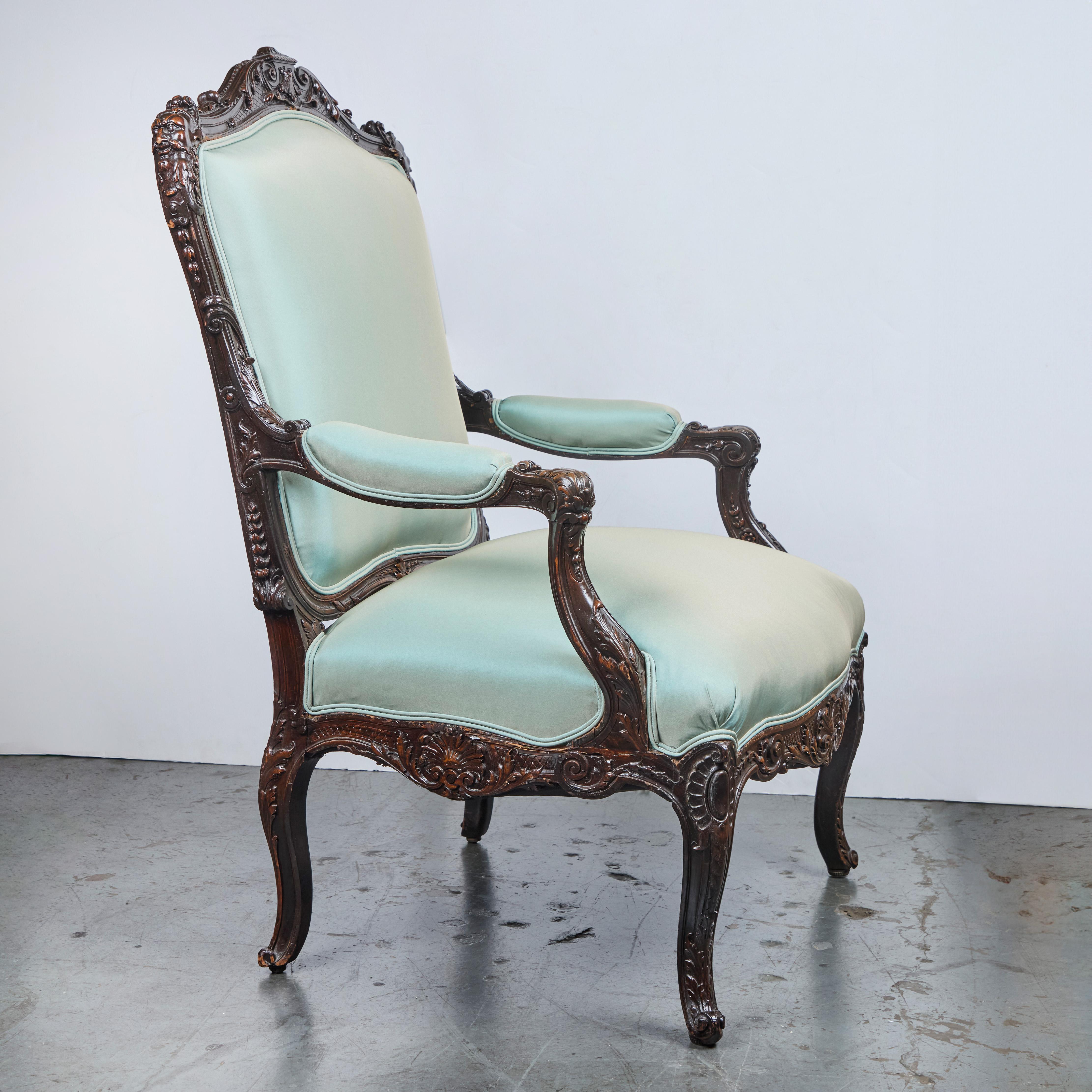 Pair of richly hand-carved walnut armchairs with faces and foliate details. 
