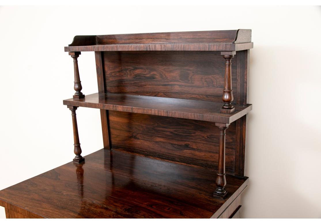 Bellissimo mobile server in legno figurato con una galleria superiore a 3/4 e supporti a colonna torniti e affusolati. Il mobile sporgente con supporti a lesena con capitelli a foglia e un'anta in vetro, un unico ripiano regolabile all'interno.