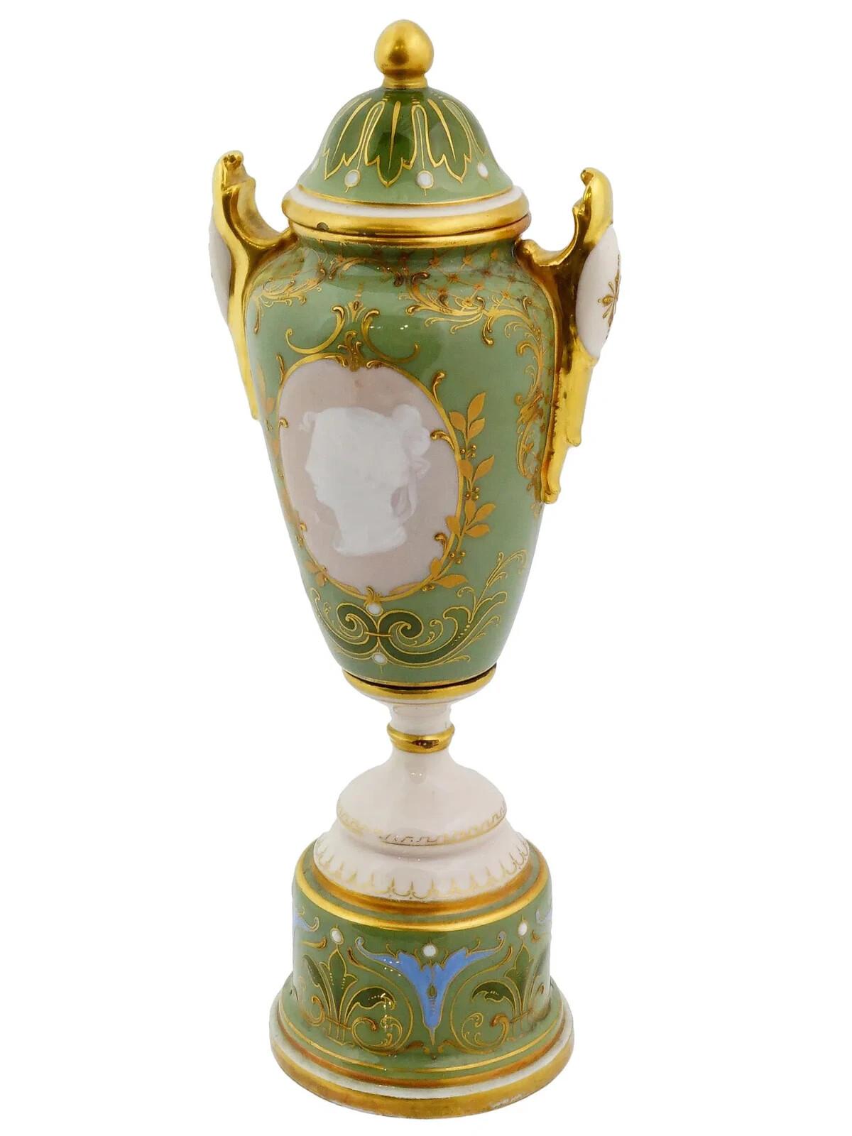 An antique Royal Vienna lidded pate sur pate, paste on paste porcelain urn vase. The vase is adorned with an image of a Neoclassical medallion portrait of a woman surrounded by a gilded foliate scroll frame. The vase is adorned with a pair of