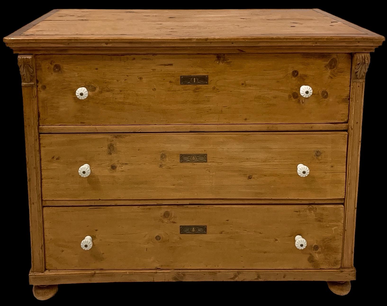 This is a large scale 19th century English carved pine chest or commode with porcelain knobs. The drawers have dovetail construction. It has age appropriate patina.