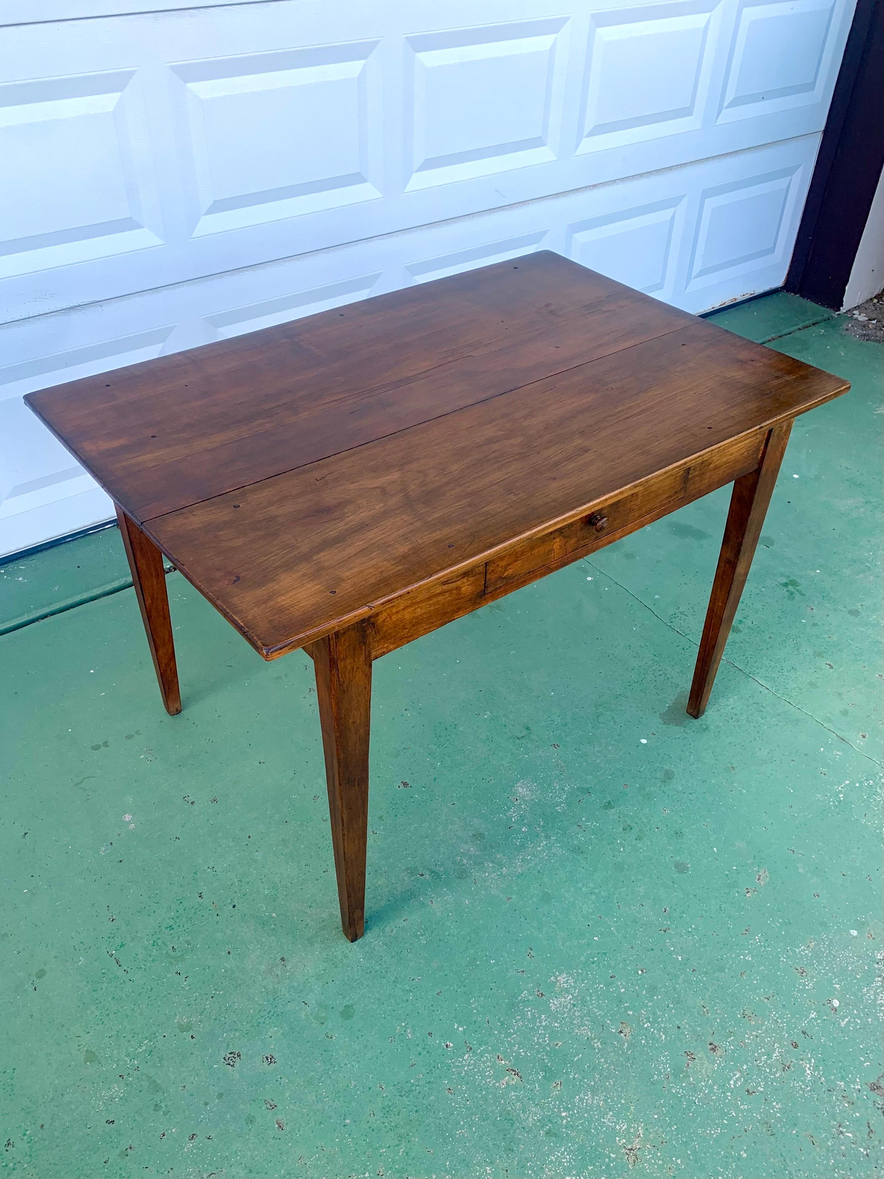 A primitive rustic farmhouse style table with a singe drawer. Top consists of two 12” wide planks with a 4.5” stretcher piece. Has wear and nail heads that show through but has a dark finish on it as well. Age is still well apparent when viewing the