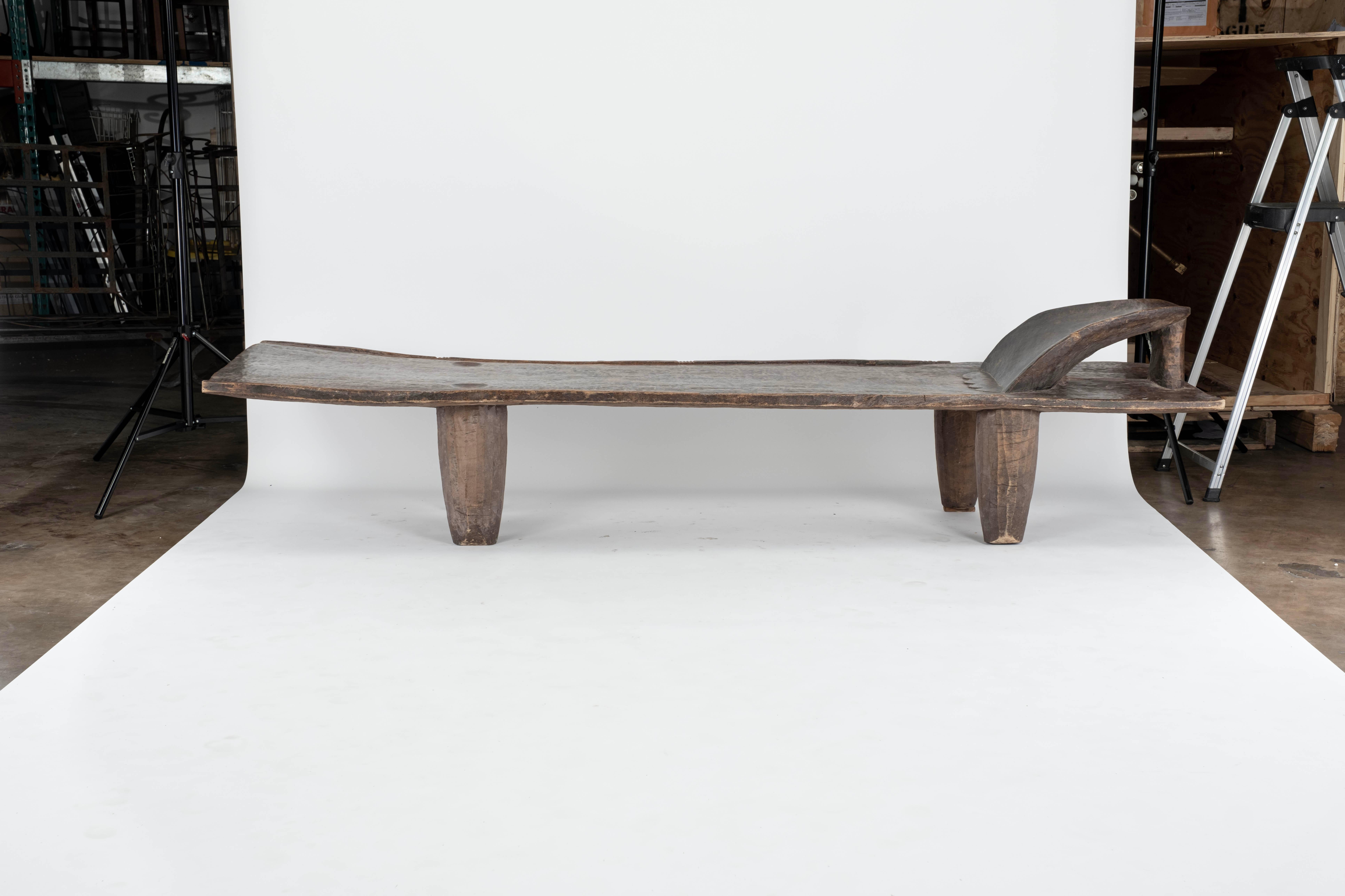 Hand carved by the Senufo tribes from a single block of iroko wood, native to the west coast of Africa. The wood is tough, dense and very durable. Shown with cone style legs and a raised headrest. Originally used as a bed that can also be used as a