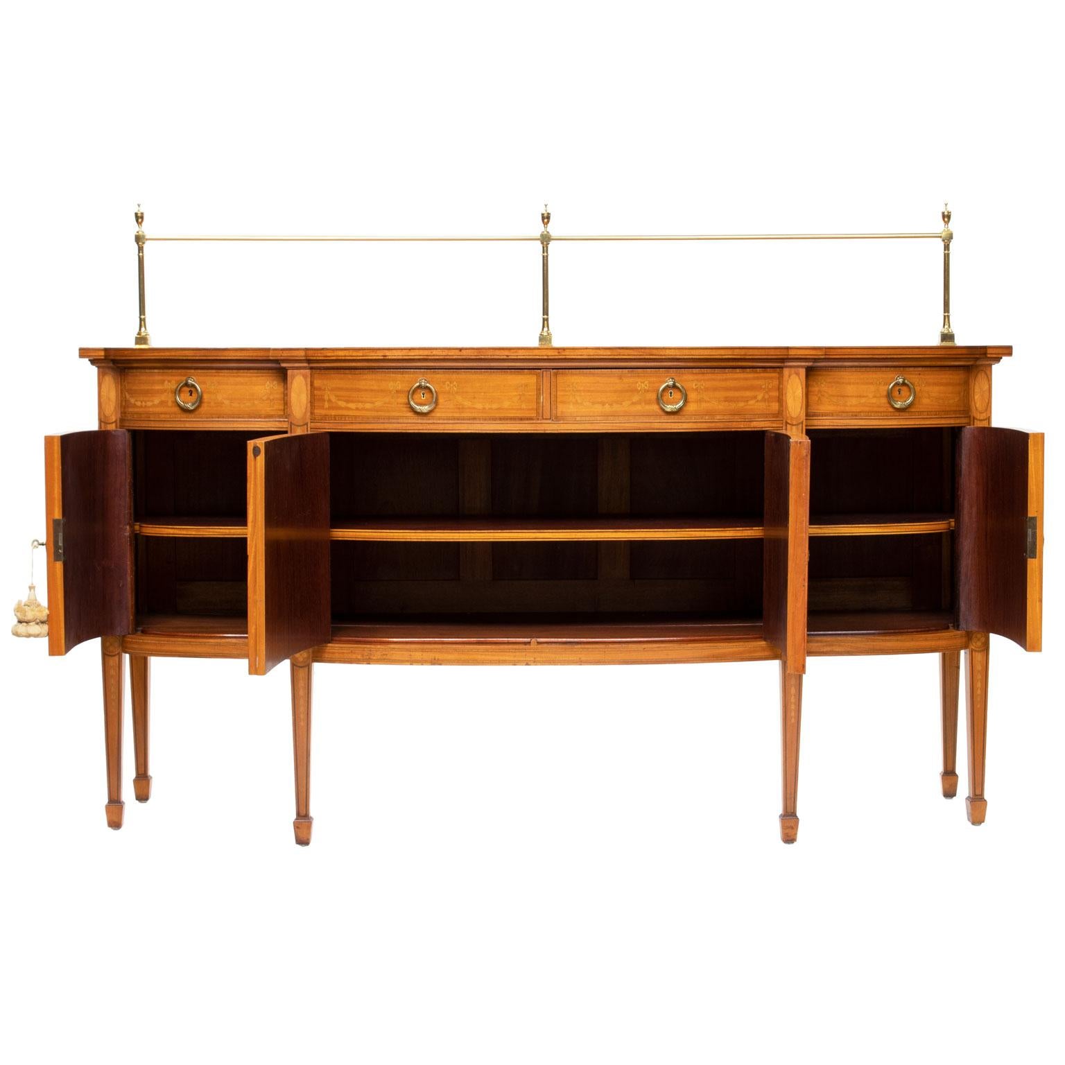 A superb 19th century Sheraton satinwood inlaid sideboard with brass gallery. The sideboard has a shaped breakfront. Very intricate inlay. There are three drawers with round laurel pulls above four-door with shelves. Each shelf finished and fronts