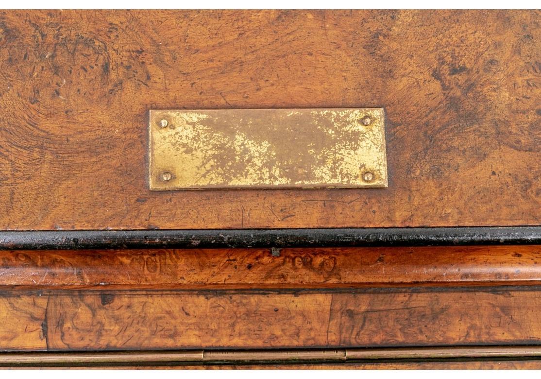 A fine Captain’s desk in particularly well chosen and colorful Burl wood with string inlaid details and ebonized moldings. The very top with a 3/4 brass gallery and worn brass plaque over a black tooled leather slant front that lifts up. The