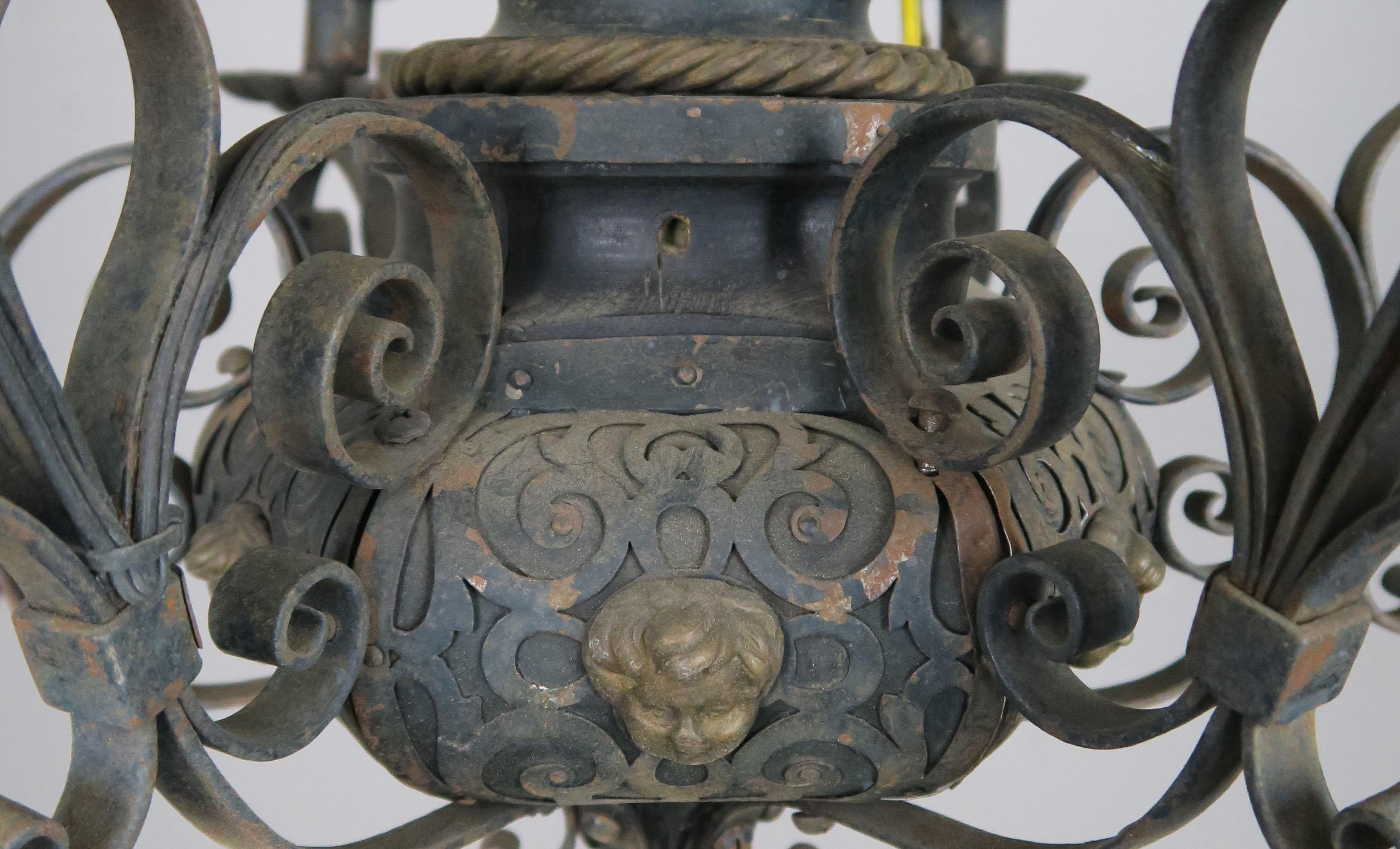 19th century six-light wrought iron chandelier intricately detailed with fleur-de-lis, scrolls, and cherub faces. The fixture has been newly wired for electricity with cream colored drip wax candle covers.