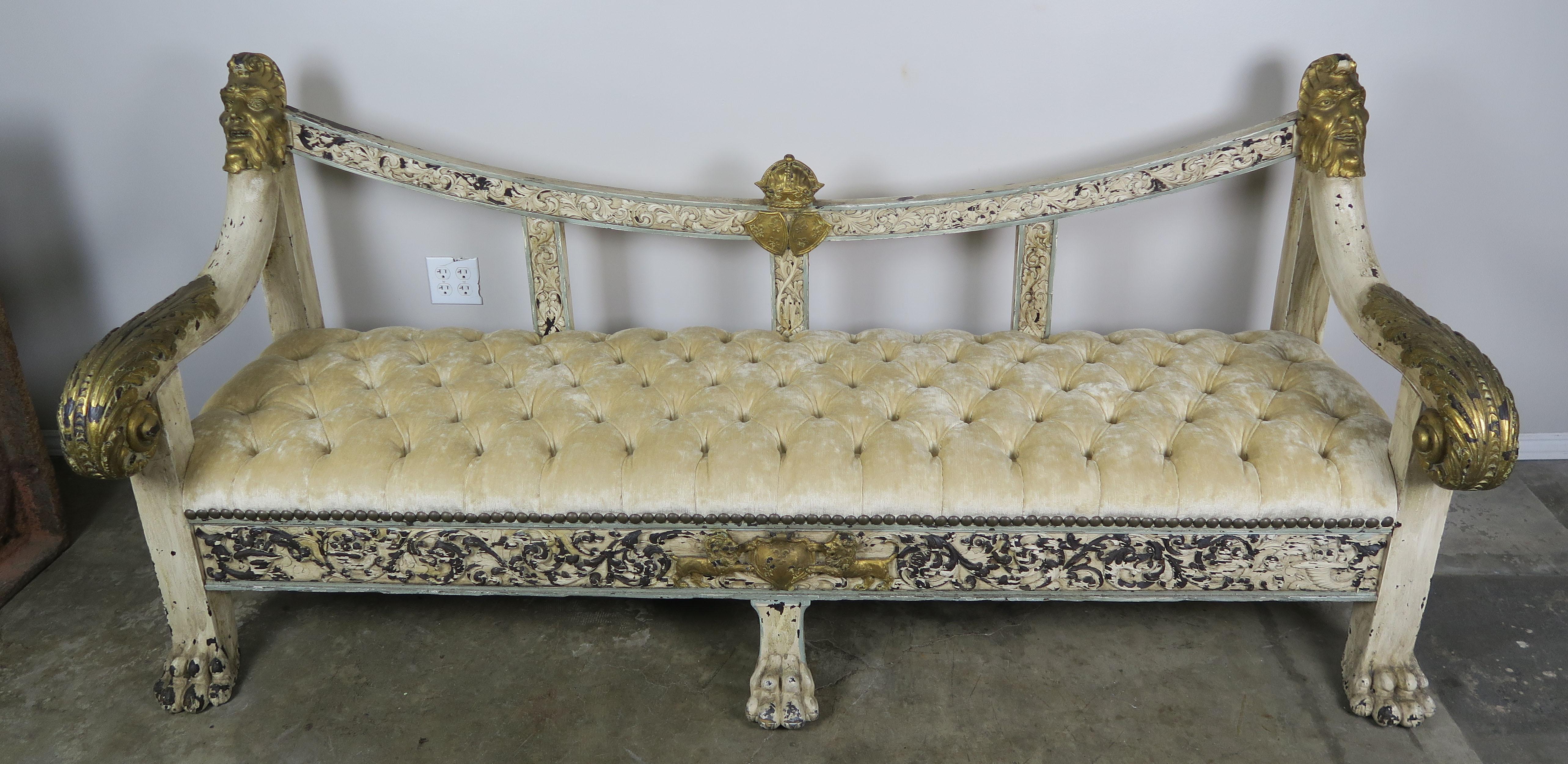 19th century Spanish Baroque style painted and parcel-gilt bench with lion feet. Beautiful carved gilt wood crown w/ pair of shields are depicted in the center of the sofa. Two detailed faces are carved at the tops of both arms and scrolled acanthus